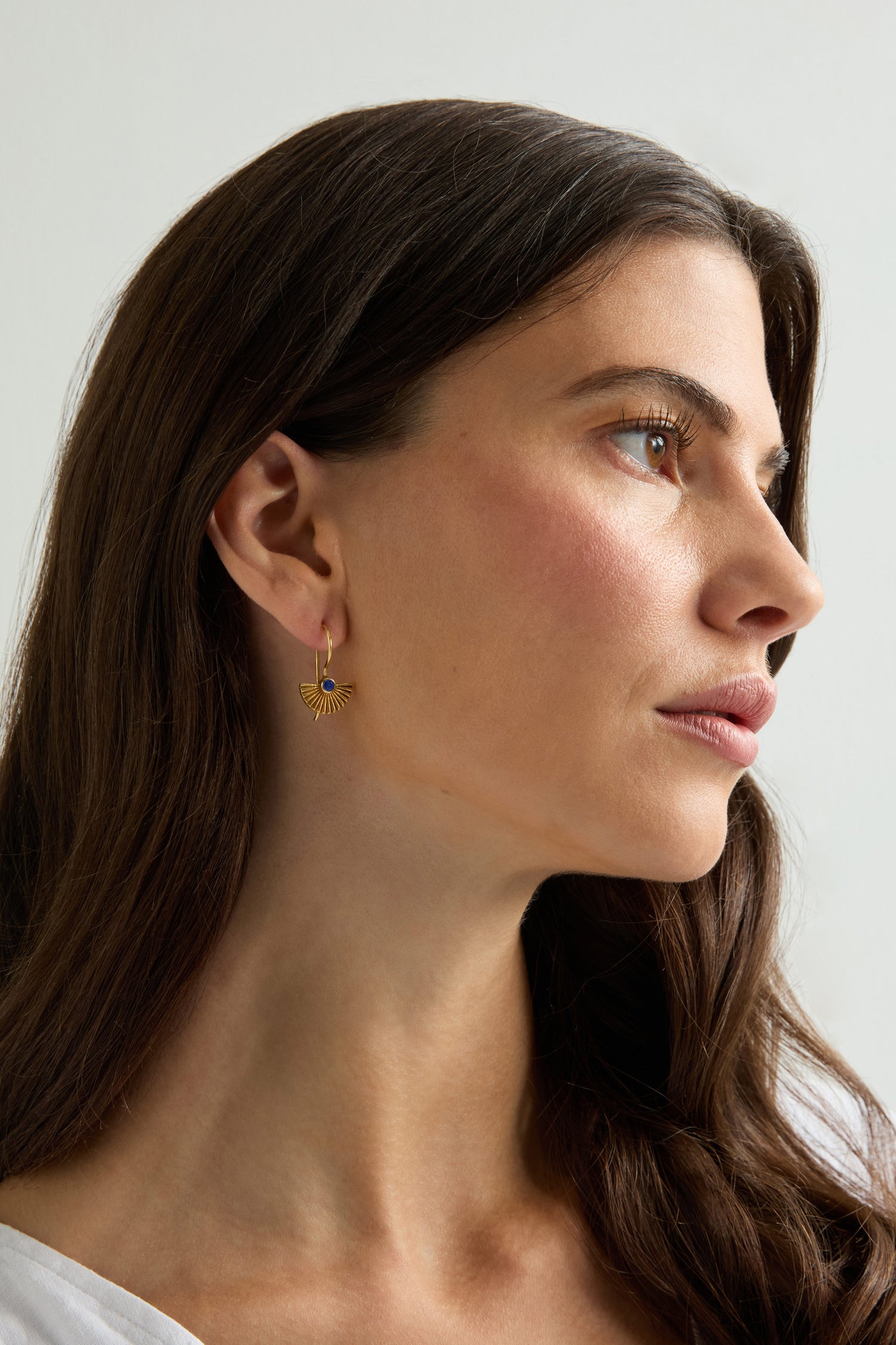 A woman with long brown hair in a white top wears Gold Vermeil Lapis Fan Earrings, looking to the side against a neutral background.