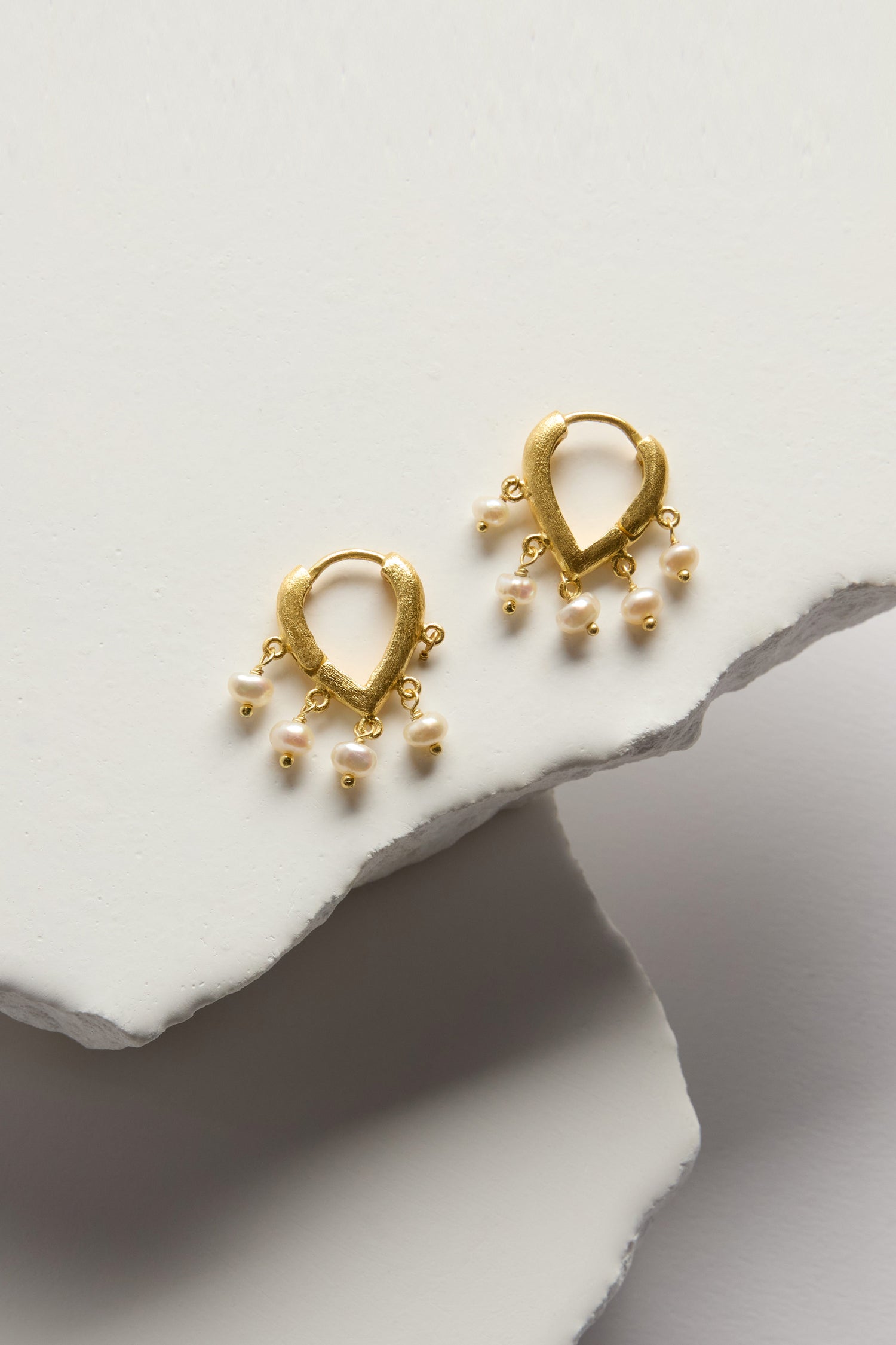 Gold Vermeil Pearl Teardrop Hoops: 18k gold vermeil clicker hoop earrings with teardrop shapes and small dangling white pearls, shown on overlapping white textured surfaces.