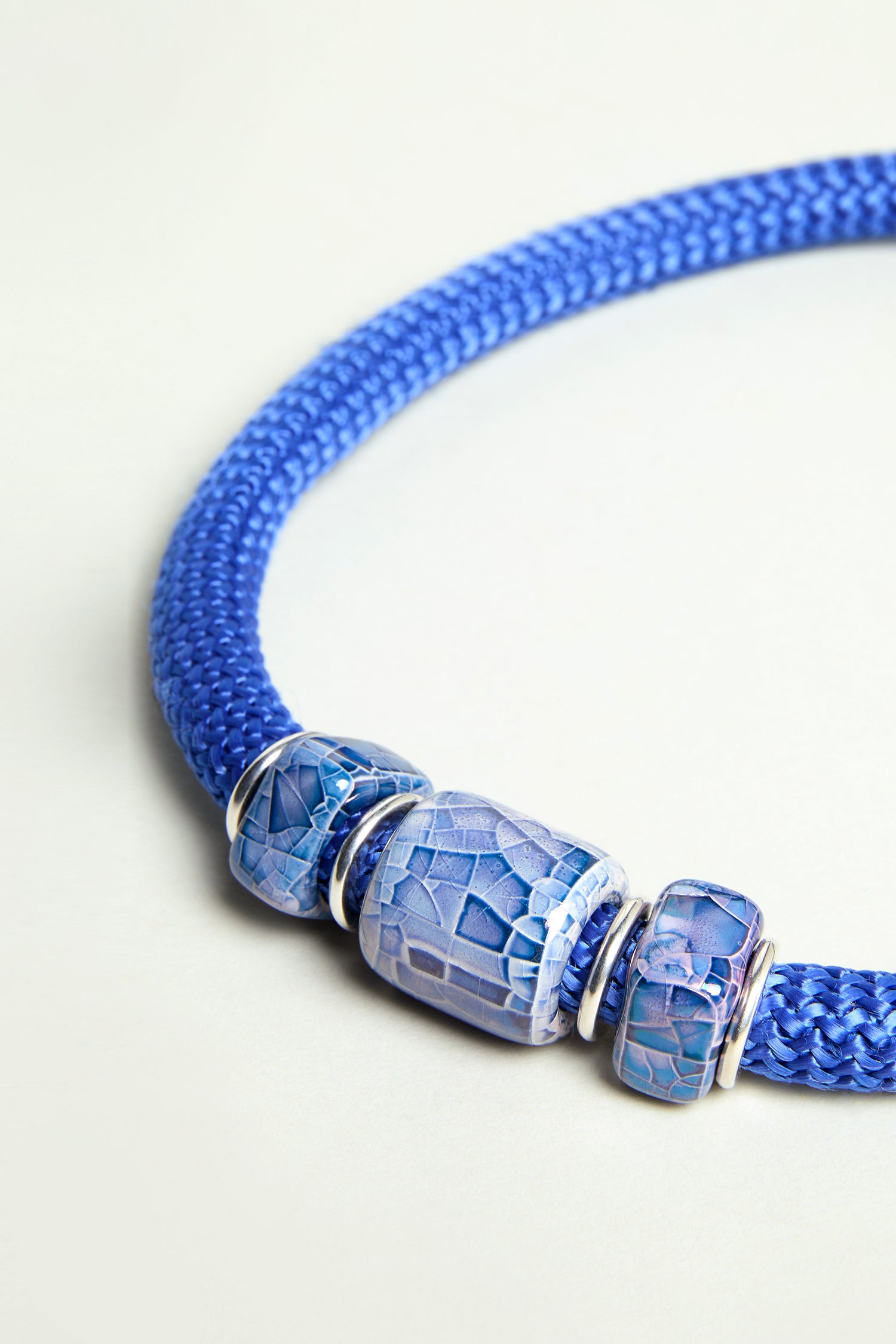 A close-up of the Triple Marble Bead Short Cord Necklace—exclusive to Sahara—showcases three striking blue and silver patterned beads, making it a perfect statement piece.