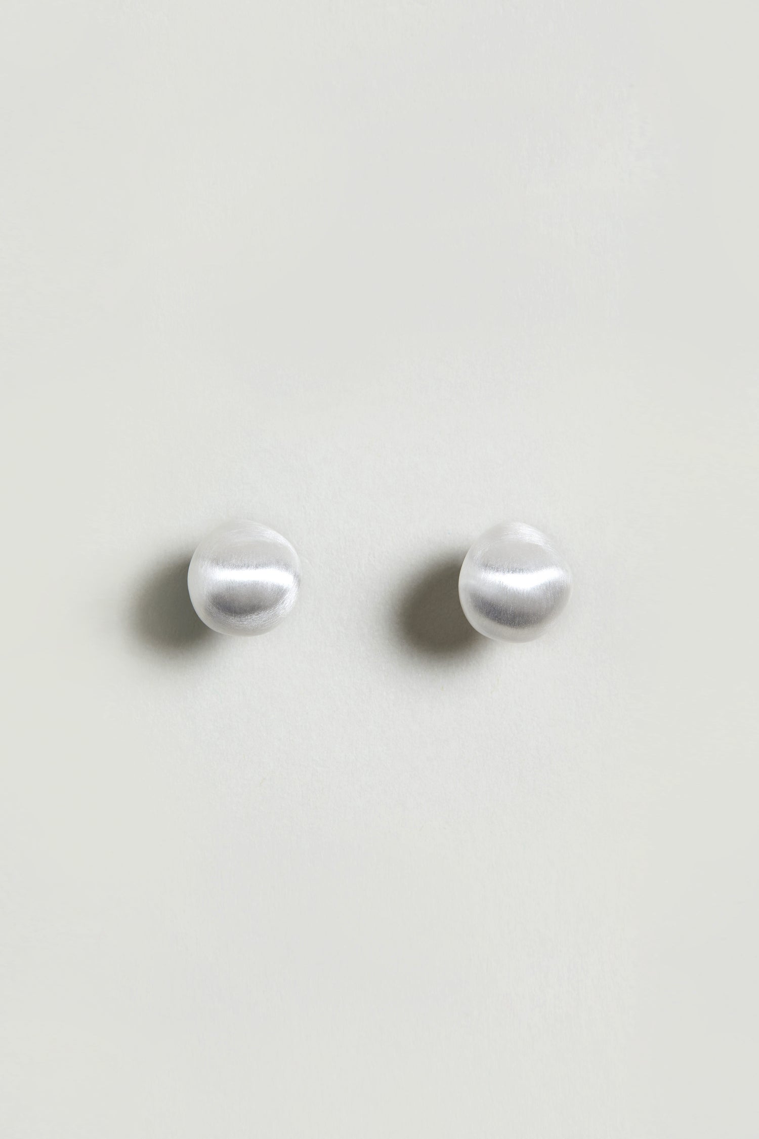 A pair of Mini Silver Pebble Earrings with a subtle silver-tone finish, displayed on a plain light background.
