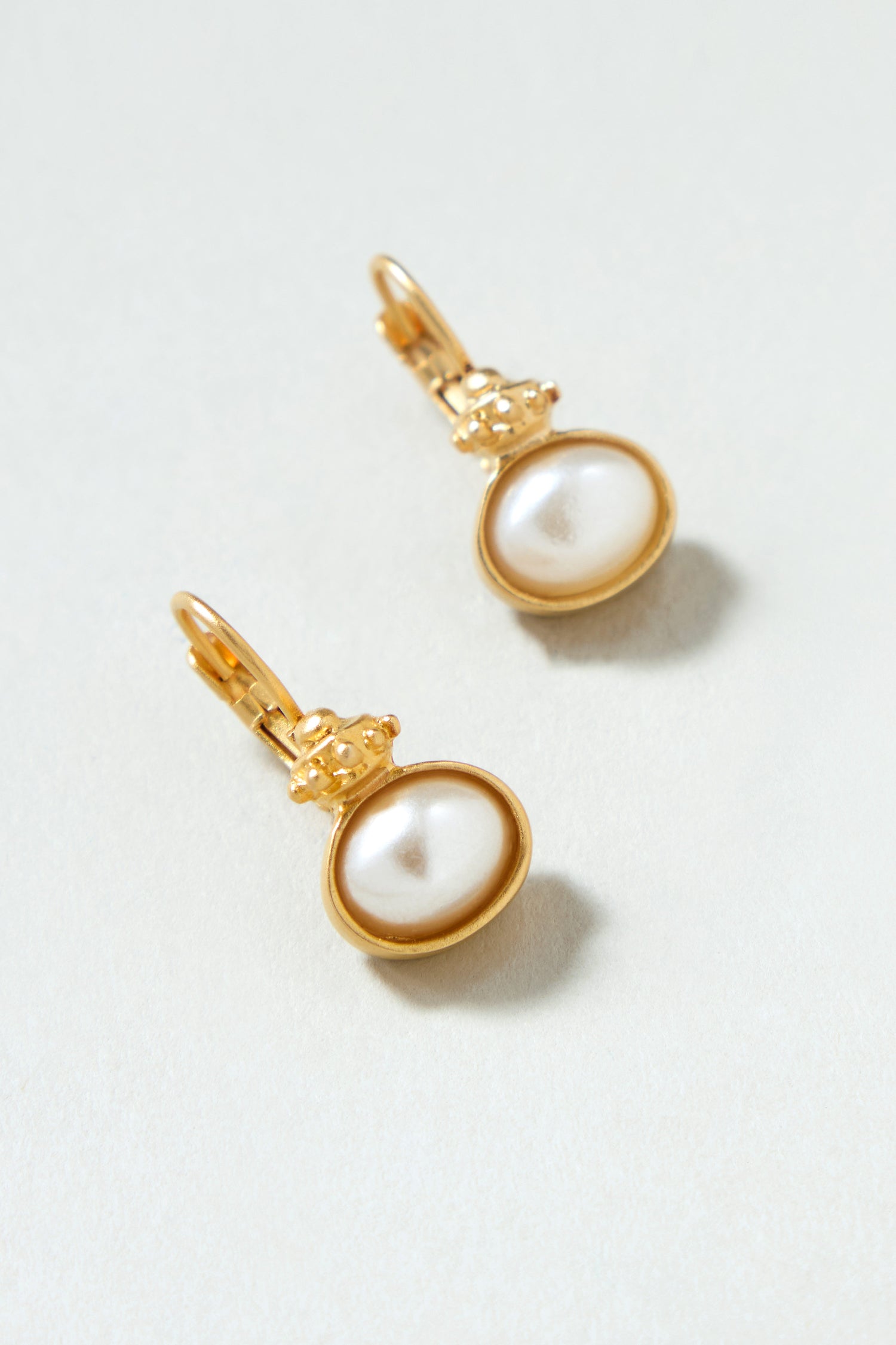 Gold Plated Pearl Drop Earrings featuring oval-shaped white pearls, shown elegantly on a light surface.
