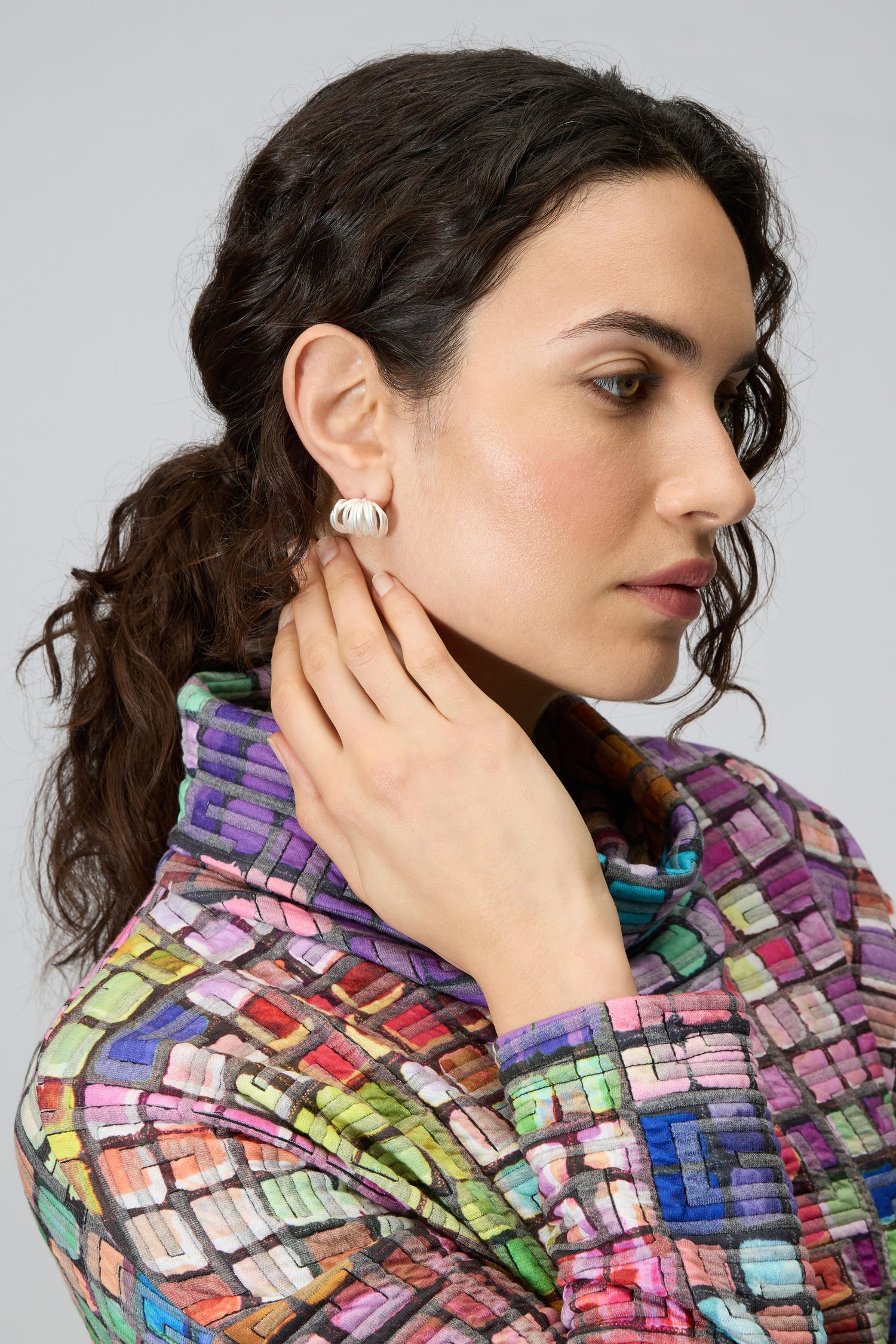 Woman with wavy brown hair, shown in profile wearing a multicolored textured top and Silver Vortex Earrings, her hand gently touching her ear.
