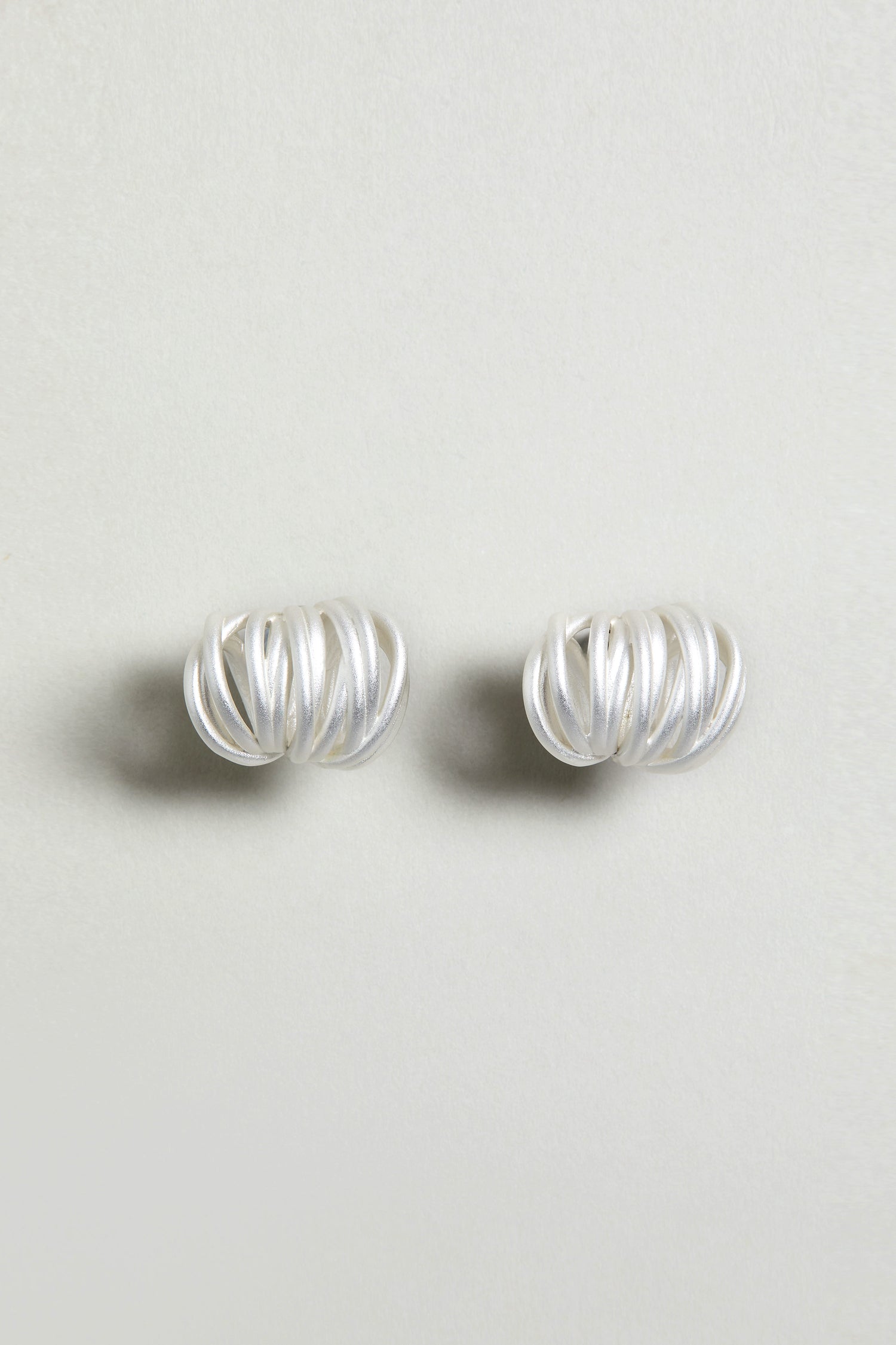 The Silver Vortex Earrings are sculptural, silver studs with a spiral shape, showcased against a simple light background.