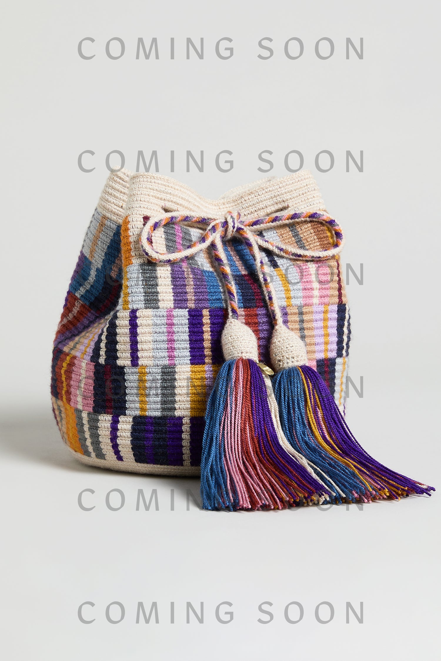 The Hand Crocheted Wayuu Crossbody Bag features a colorful woven design, drawstring closure, and two large tassels. Displayed on a plain background with "COMING SOON" text—item code GNG12W00013332.