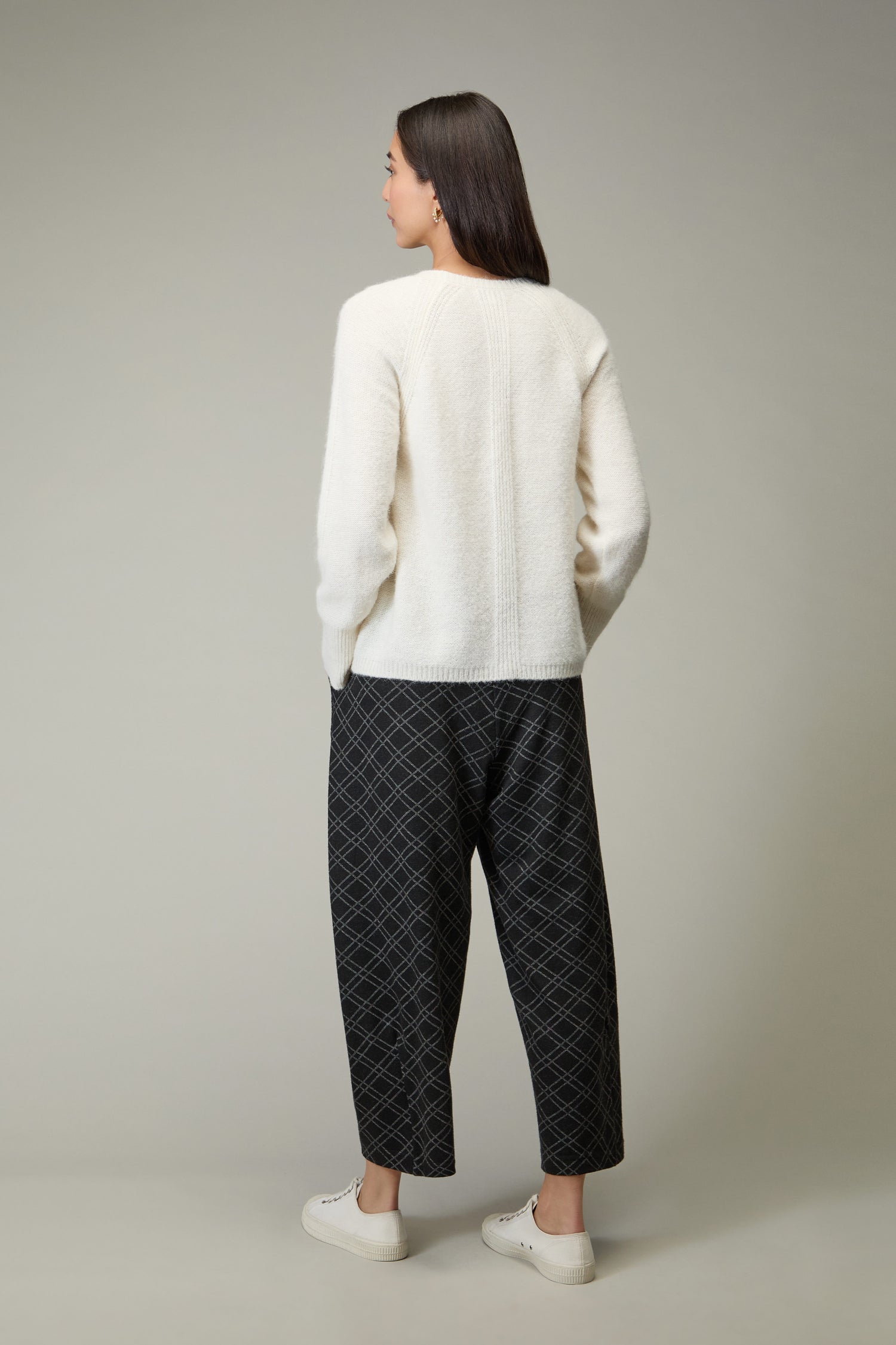A woman faces away, wearing the Alpaca Blend Seam Detail Jumper, loose black plaid pants, and white sneakers against a plain background.