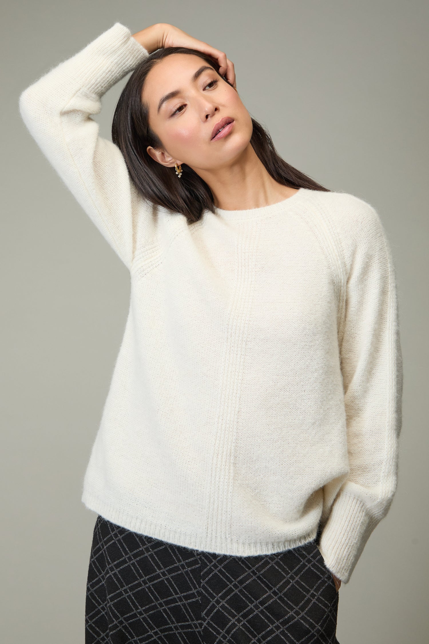 A woman in the Alpaca Blend Seam Detail Jumper and dark plaid pants stands against a plain background, one arm resting on her head.