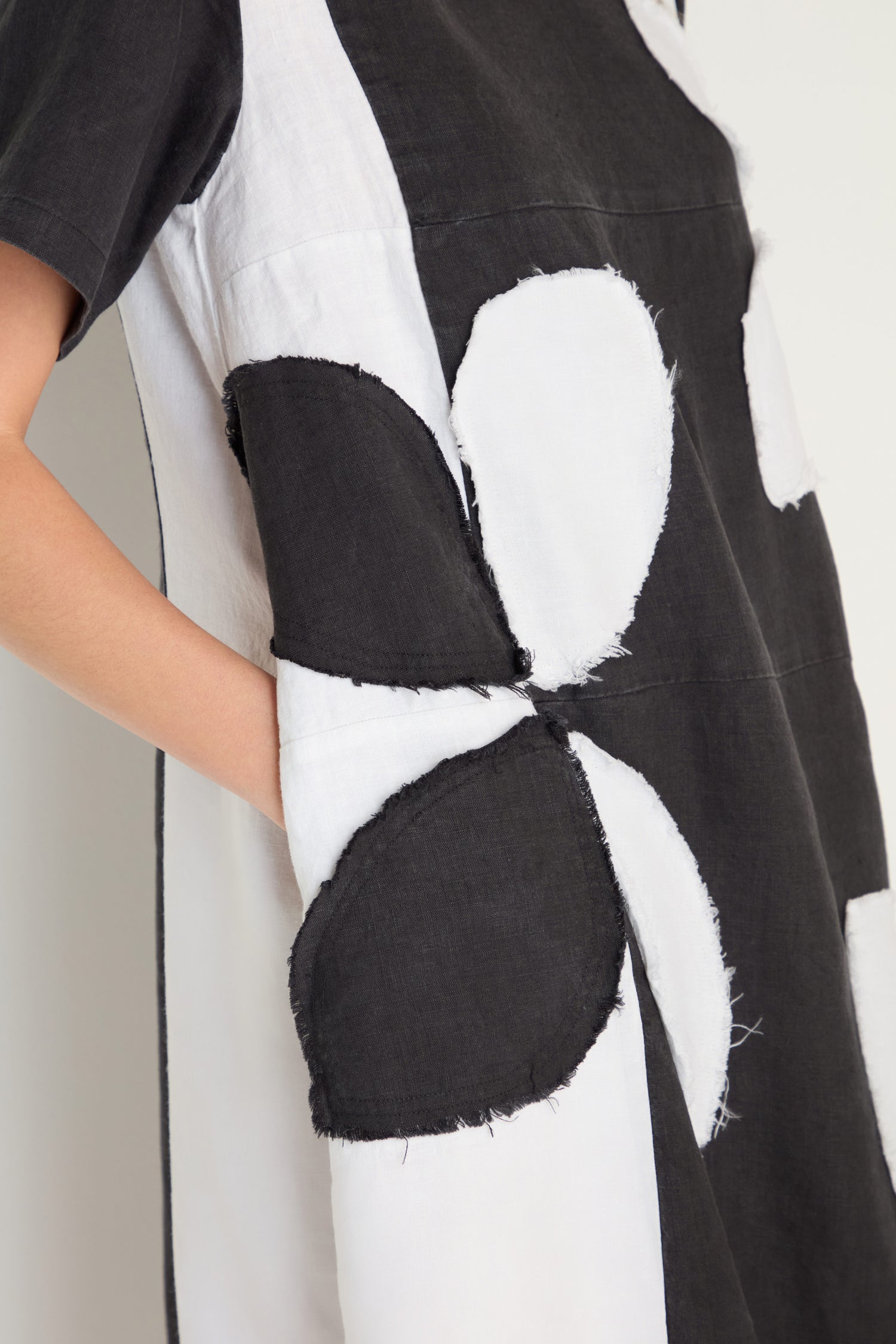 Close-up of the Quant Monochrome Linen Dress, showcasing bold rough-edged floral appliqué patterns and a visible side pocket.