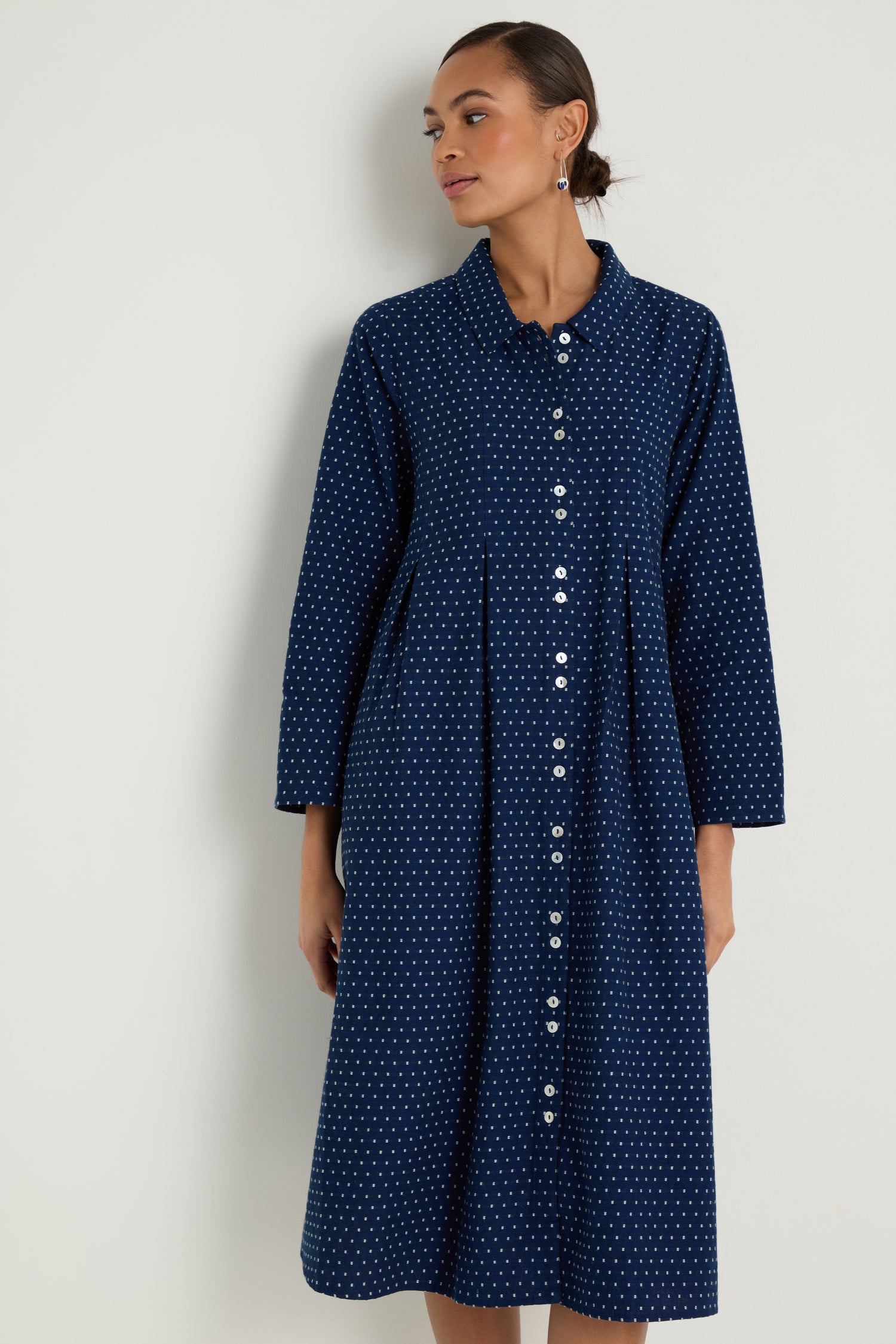 A woman models the Indigo Spot Cotton Shirt Dress—navy blue with white polka dots, long sleeves, a relaxed A-line silhouette, and crafted from cotton—against a plain light background.