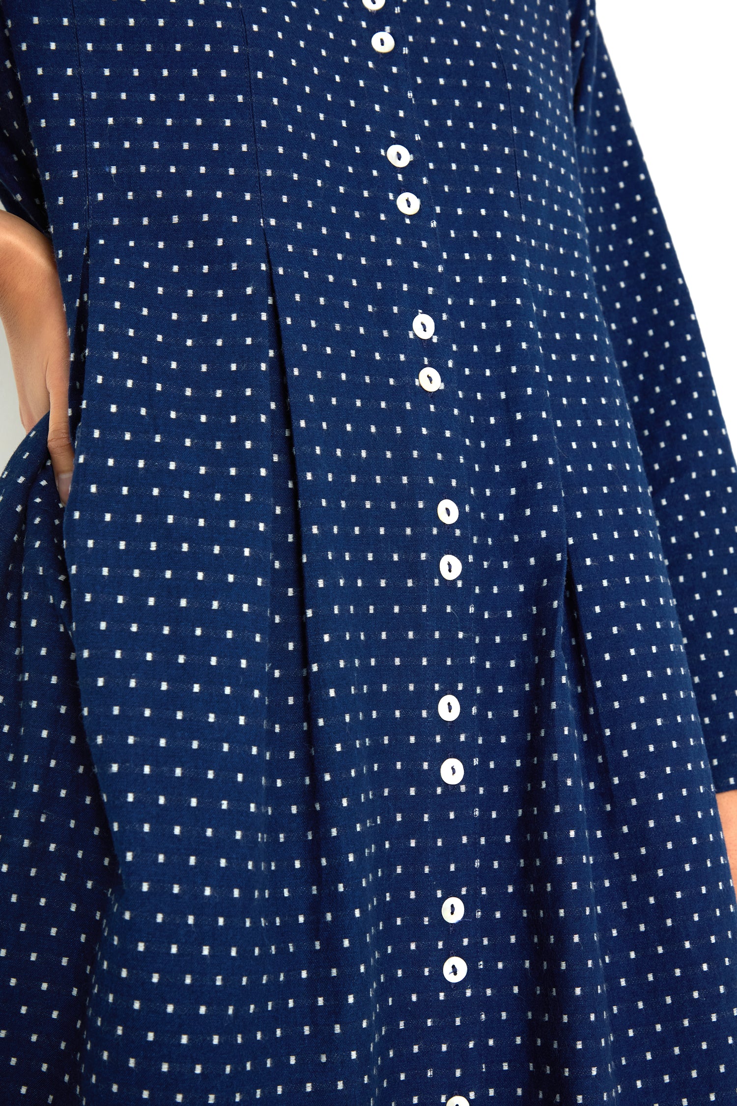 Close-up of the Indigo Spot Cotton Shirt Dress—blue with white polka dots, front white buttons, A-line silhouette, and side pocket with a hand tucked in.