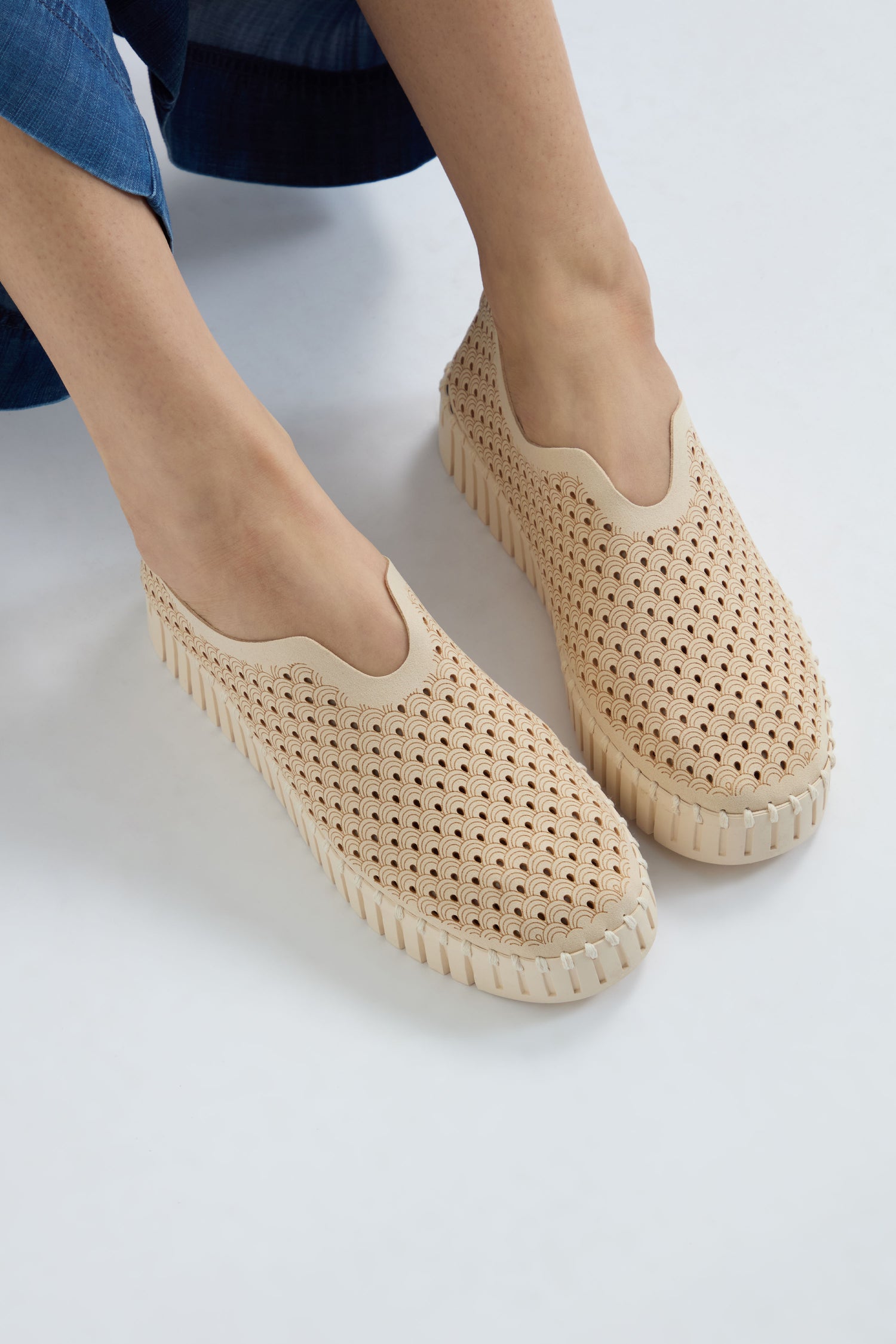A person wears beige Tulip Slip On Shoes by Ilse Jacobsen, featuring perforated scalloped patterns and a platform sole, against a plain background.