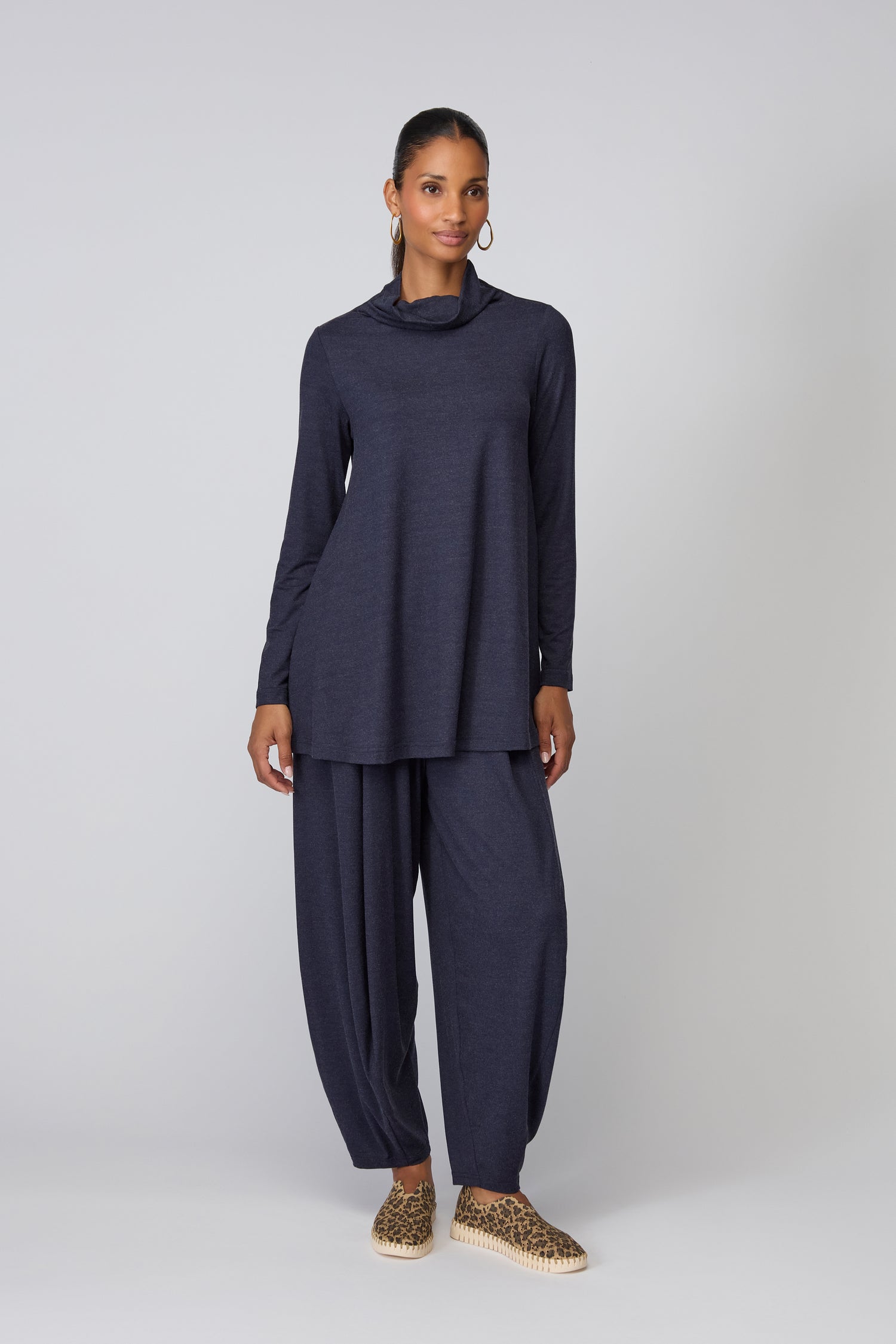 A person stands against a plain background wearing a loose-fitting navy top, matching wide-leg pants, and Tulip Leopard Slip On Shoes for a bold accent.