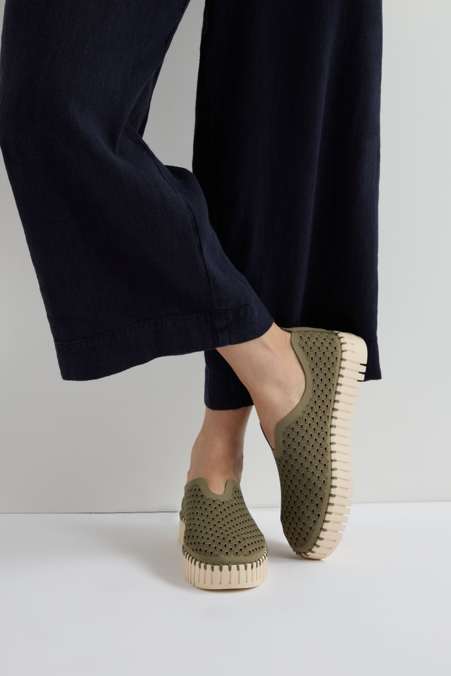Person wearing black wide-leg pants and Khaki Tulip Platform Slip On Shoes with perforated uppers and light-colored soles, standing against a plain background.