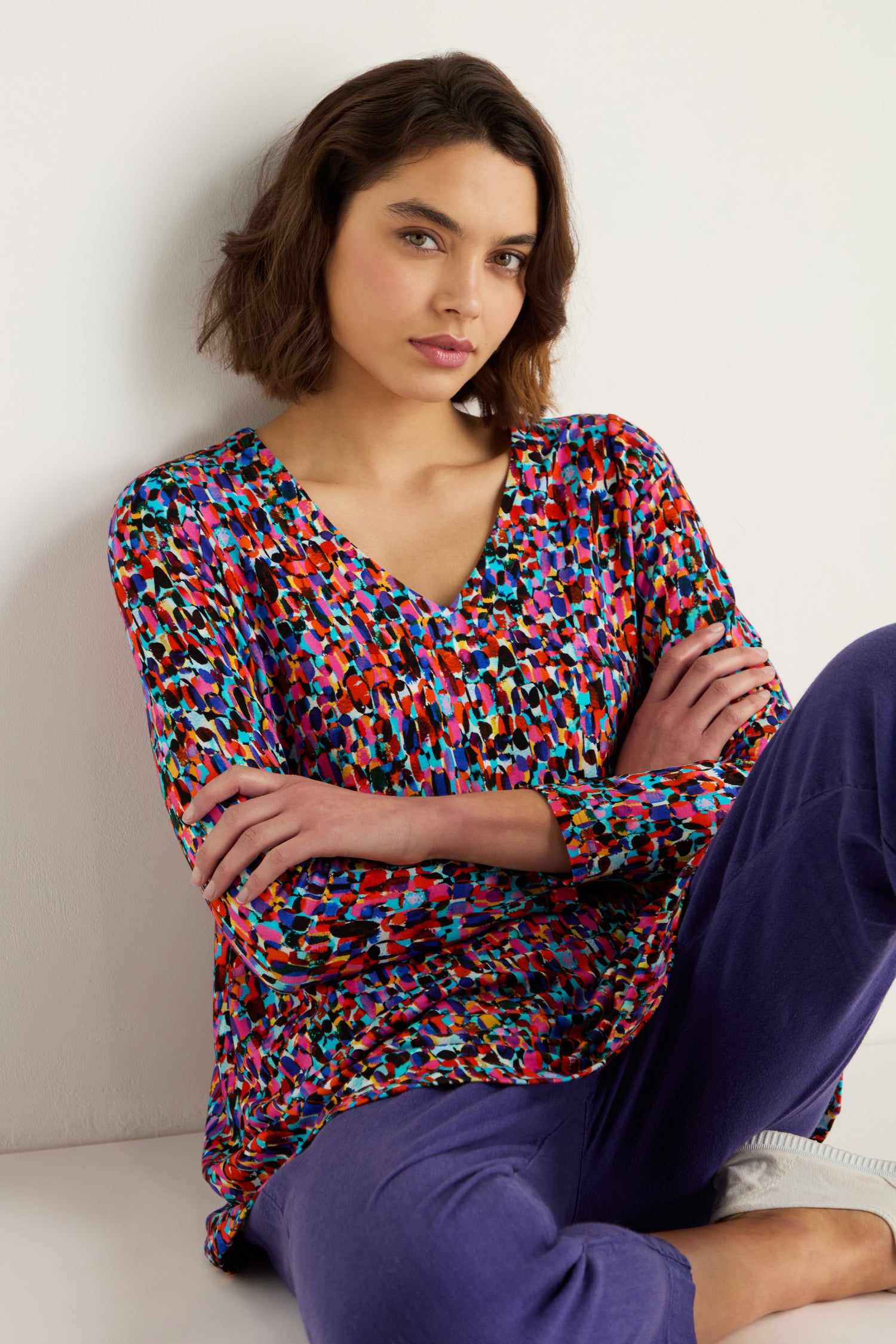 Woman sitting with arms crossed, wearing the Painted Spots Jersey Tunic and purple pants, against a plain light-colored background.
