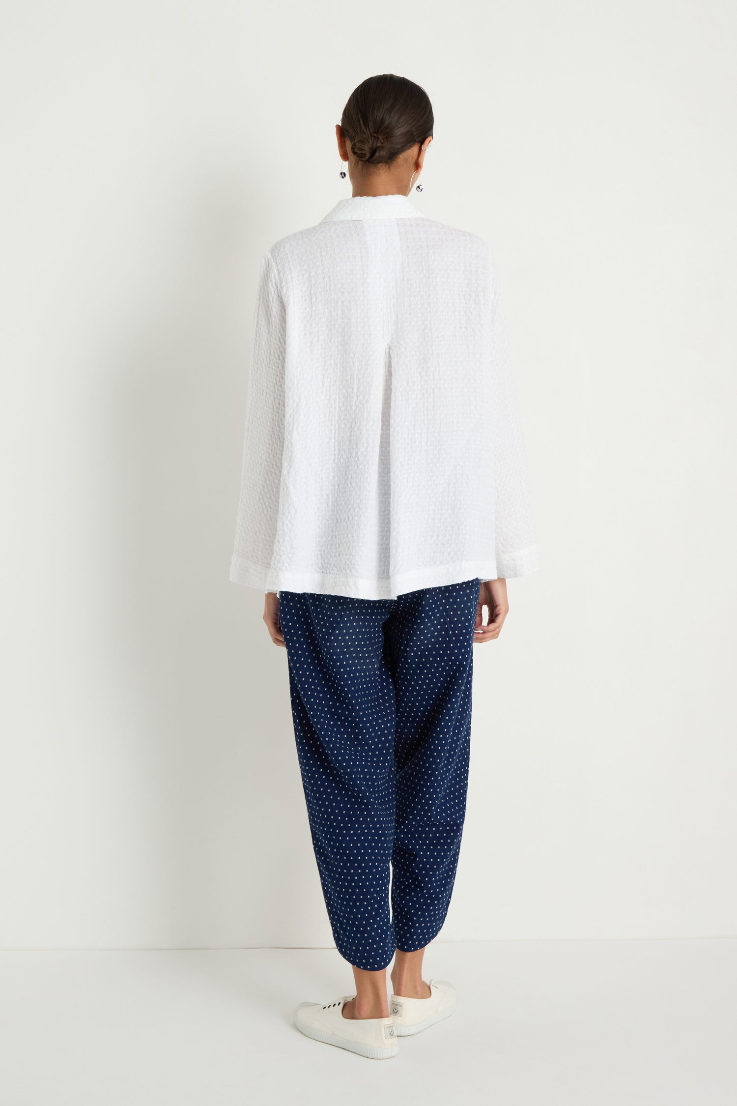 A person faces away, wearing the Waffle Linen Pocket Shirt, navy blue polka dot pants, and white slip-on shoes against a plain white background for an effortlessly breathable layered look.