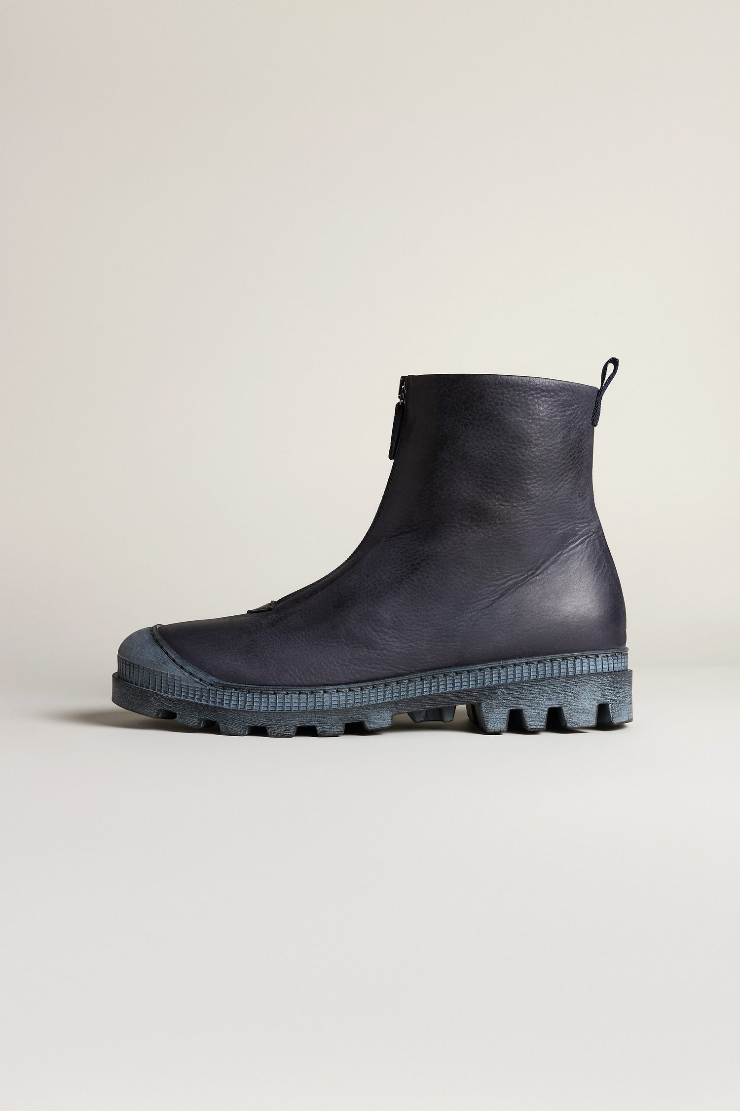 The Navy Zip Front Leather Boots feature a sleek leather design with a front zipper and a sturdy, textured sole, showcased against a plain light background.