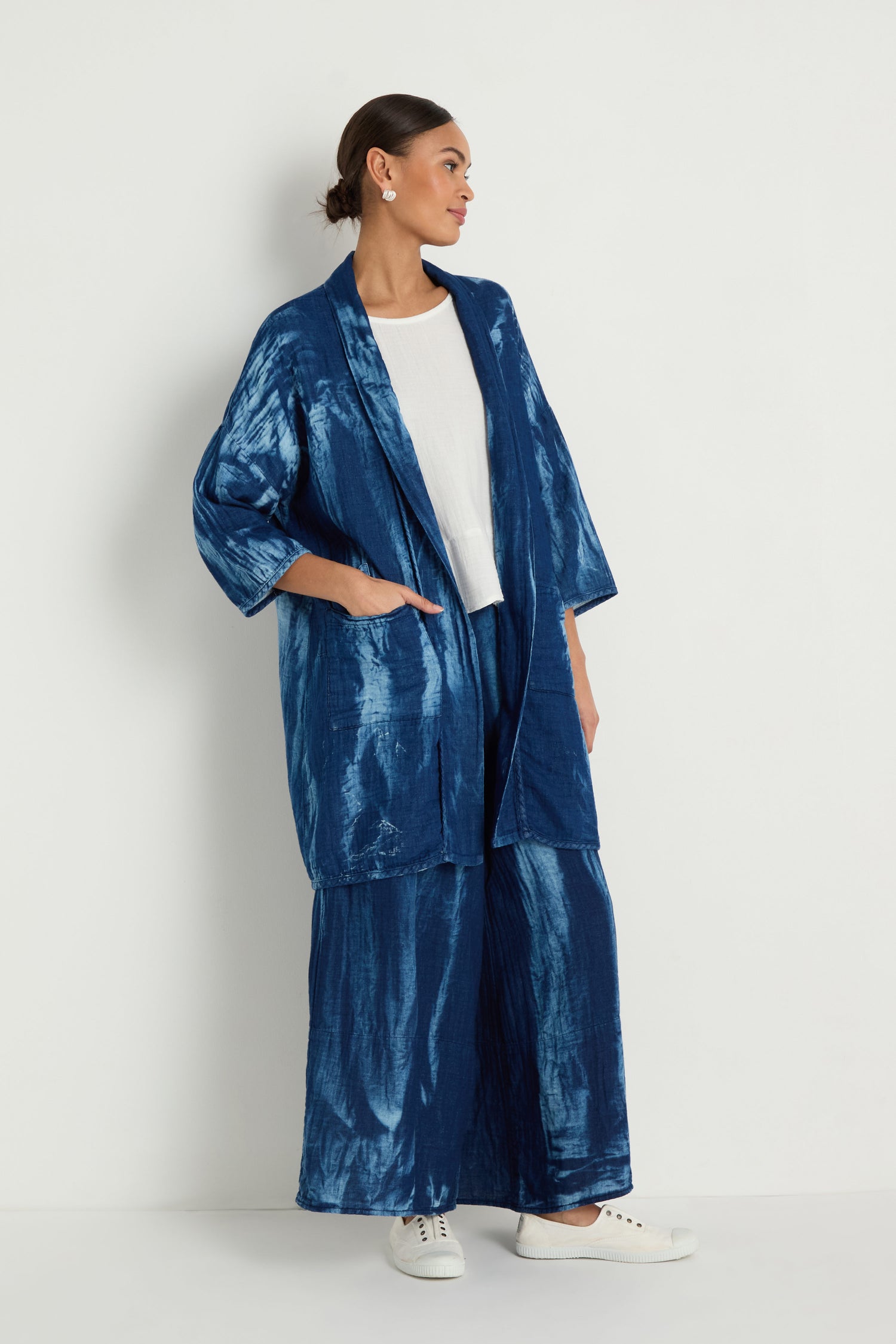 A woman stands against a white background, wearing a Soft Denim Easy Jacket with matching wide-leg pants, paired with a white top and white sneakers.