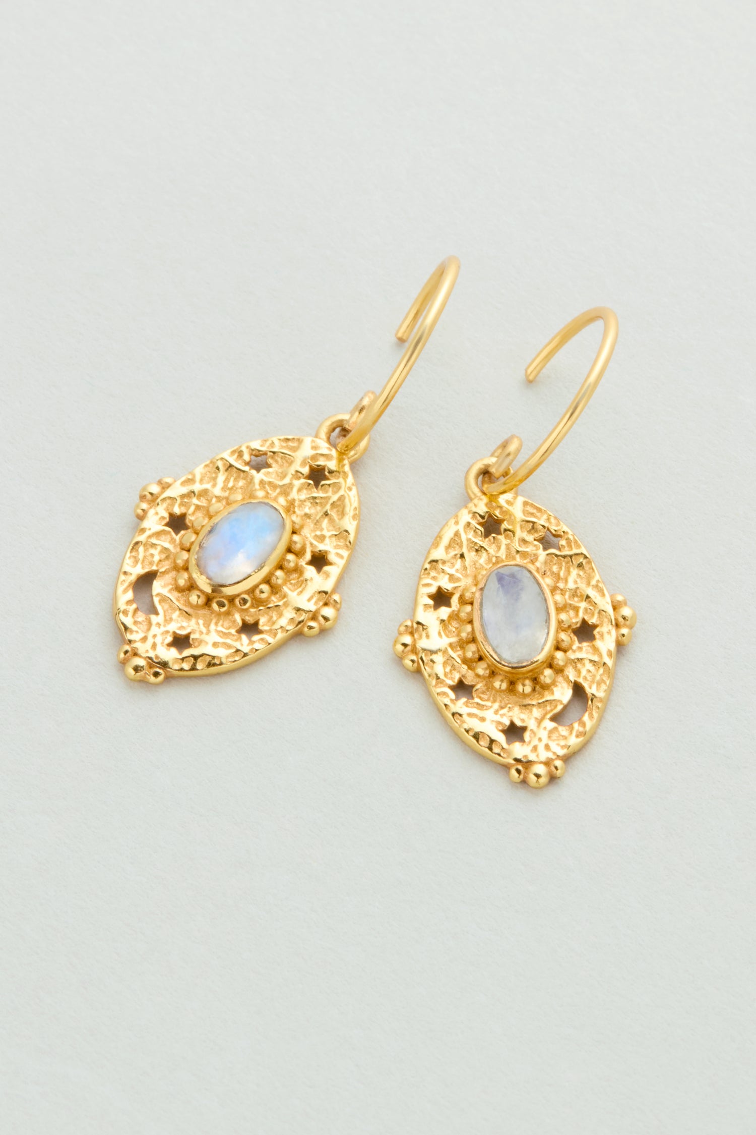 Gold Plated White Moonstone Orion Earrings (style MJU10965GB1) feature oval iridescent stones set in textured, ornate gold frames, displayed on a light background.