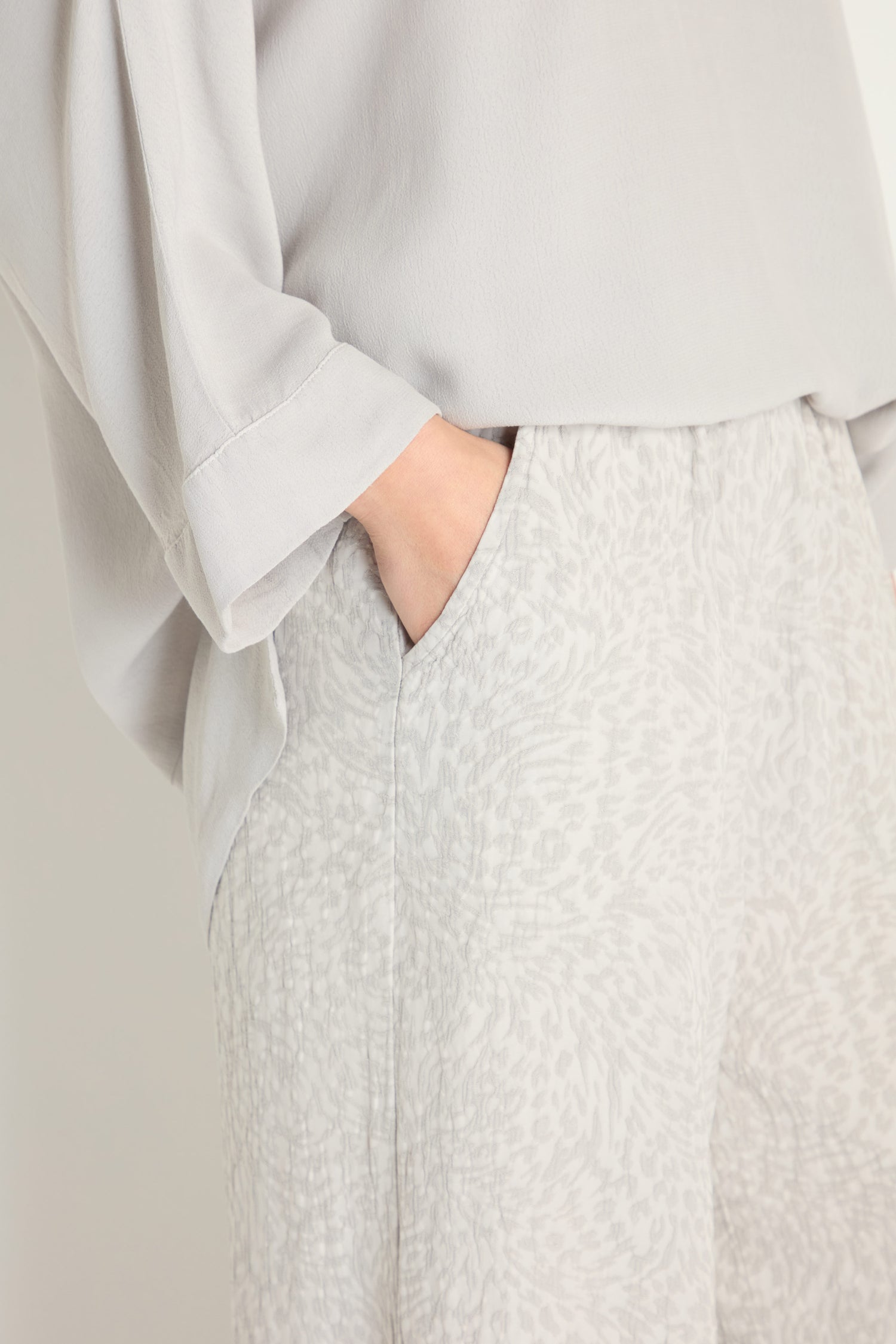 Person wearing a loose, light gray long-sleeve top and Animal Textured Jacquard Wide Trouser in light gray with one hand in the trouser pocket.