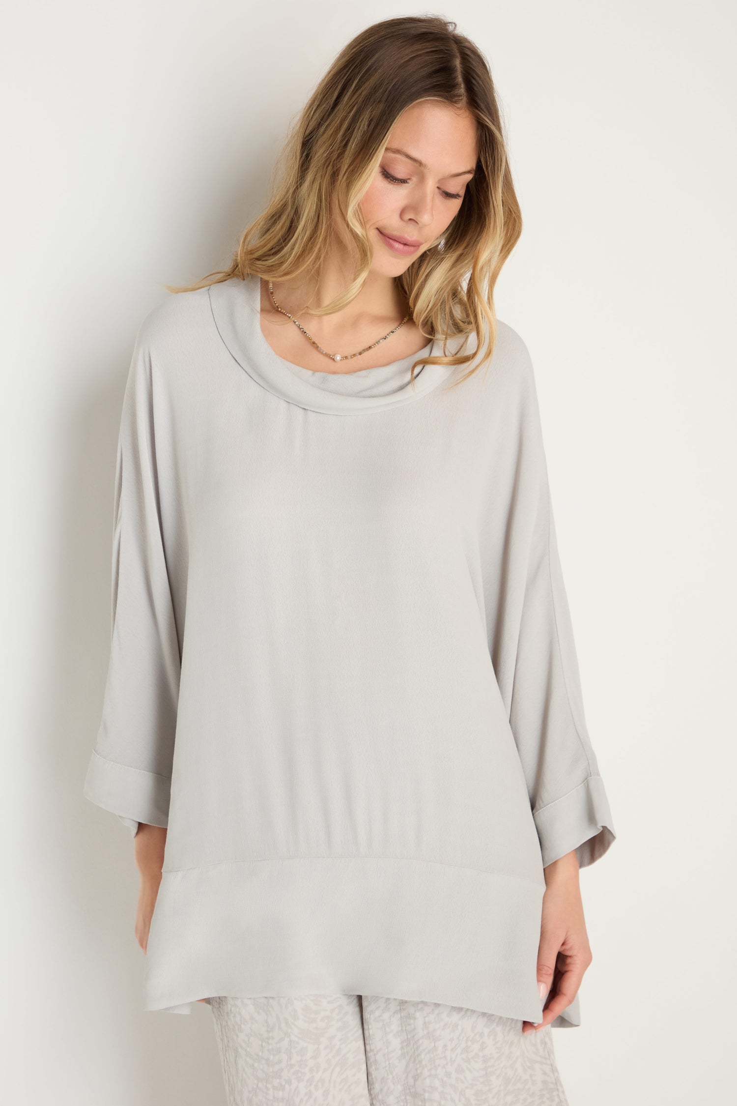 A woman wears the Crepe Boxy Top, a loose-fitting light gray long-sleeve style with cuffed sleeves (MTT5245-LVC), standing against a plain white background.