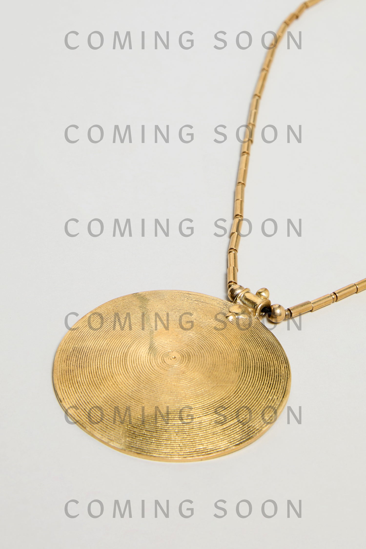 The Long Spiral Pendant (model NCCCE170) features concentric engraved lines on a gold circular pendant with a gold chain, displayed on a light background with repeated "COMING SOON" text overlay.