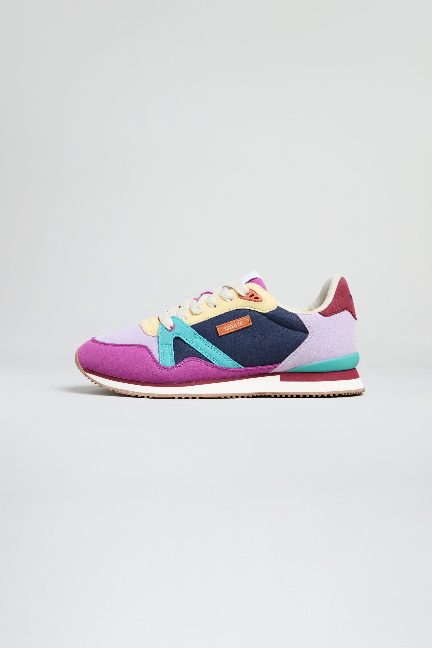 The Colour Pop Andree Trainers are vegan sneakers with bold colour-blocking in purple, blue, yellow, maroon, and black panels, white laces, and a rubber sole—shown on a plain light background.