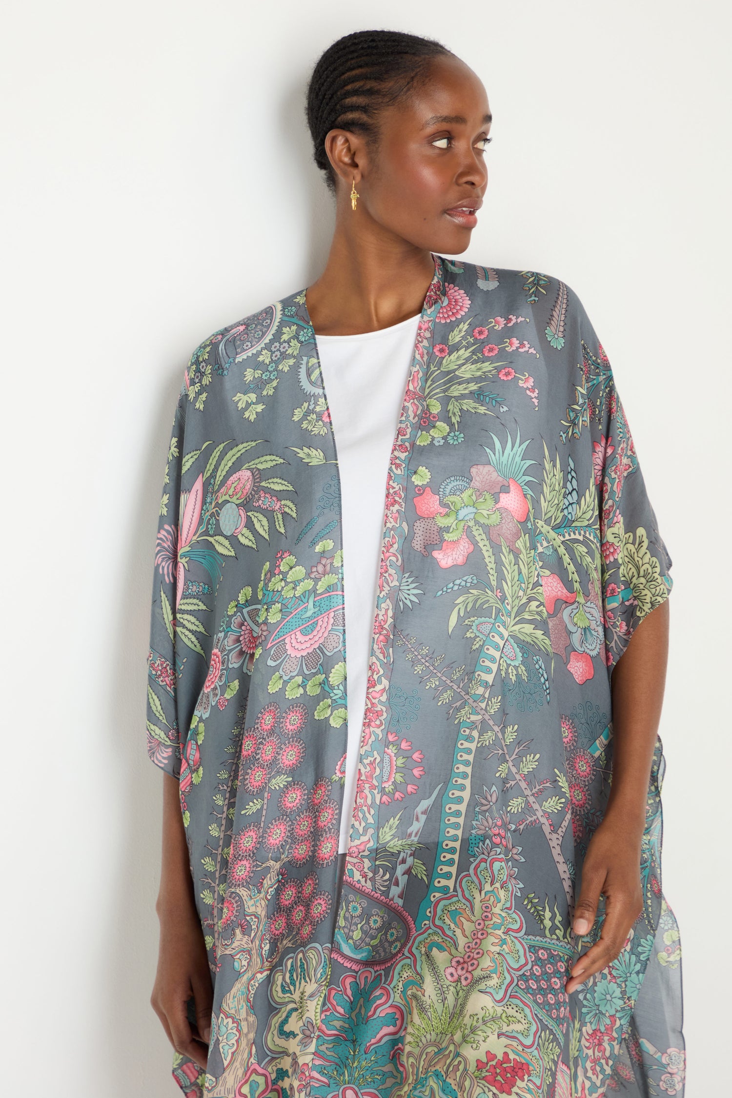 A woman wearing a Boho Garden Print Throwover over a white top stands against a white background, looking to the side.