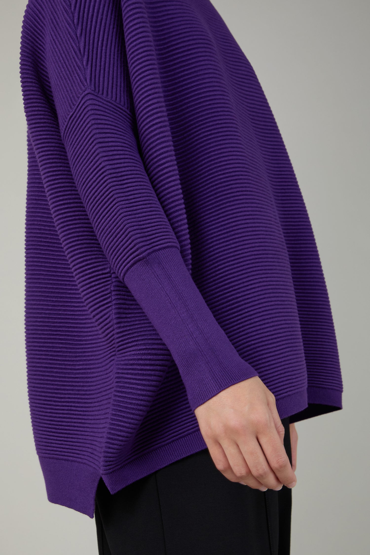 A person wears a loose-fitting, viscose-rich Ribbed Jumper in purple with long sleeves and black pants, shown from shoulders to mid-thigh against a plain background.