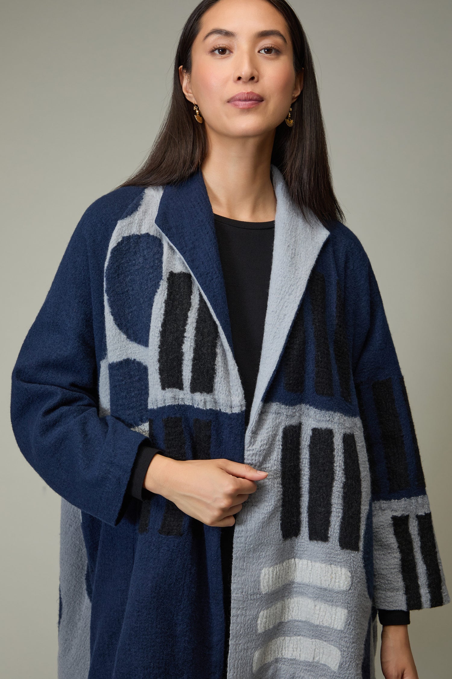 A woman with long dark hair wears the Spot and Dash Wool Jacket, featuring a blue and gray abstract pattern, over a black top against a plain background.
