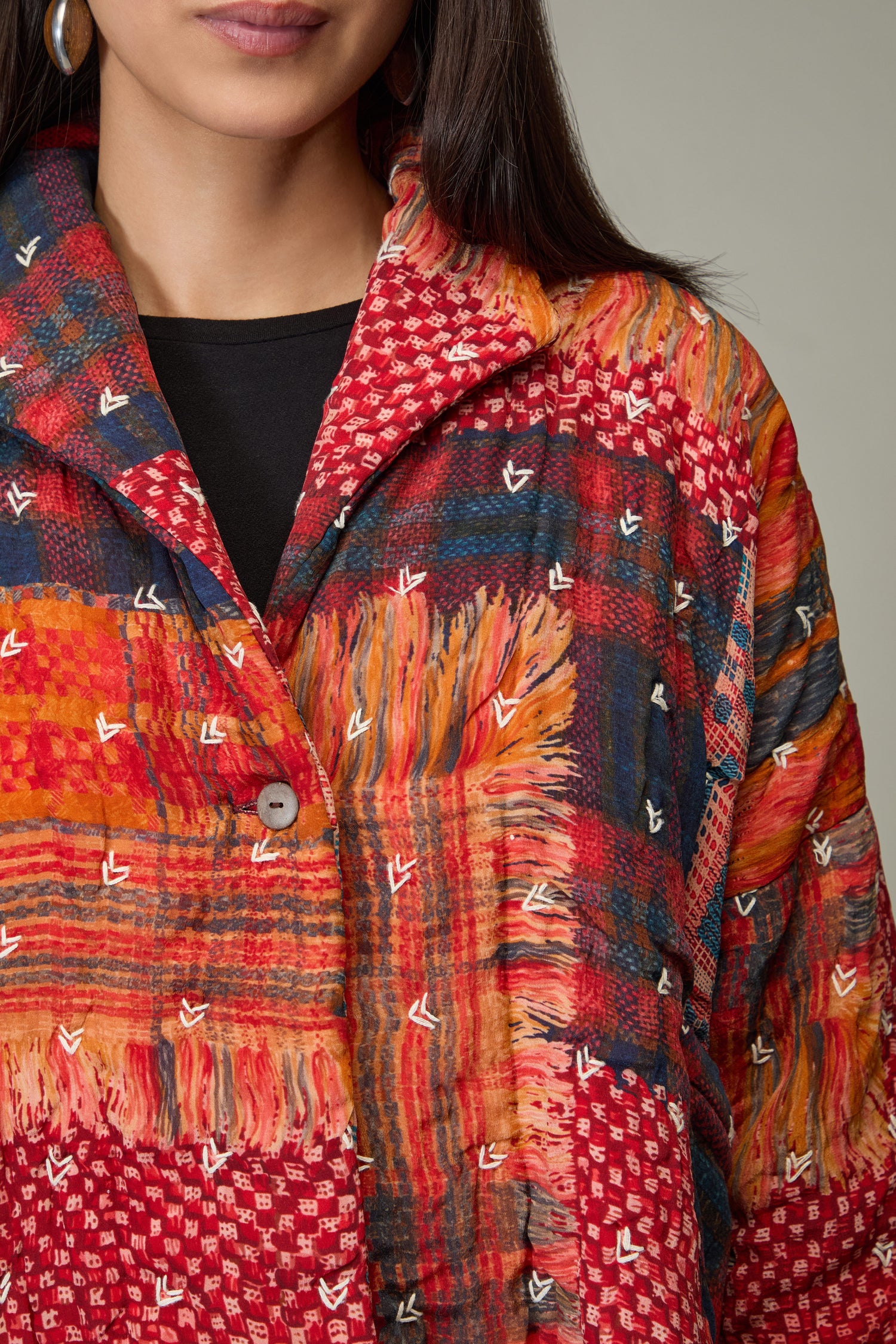 A woman wearing the Padded Multi Check Padded Jacket, featuring colorful red, orange, and blue plaid patterns and embroidered details, photographed from the shoulders up.