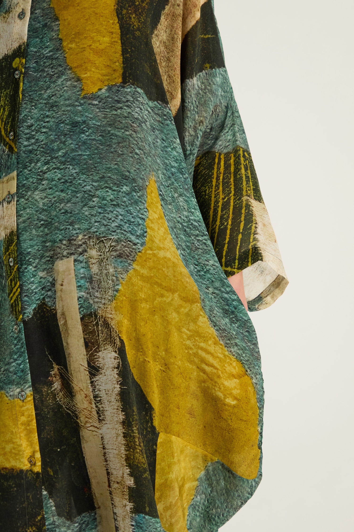 Close-up of the Ochre Print Shirt Dress, featuring painterly blue, yellow, black, and beige prints; a partial view of an arm highlights its artistic flair.