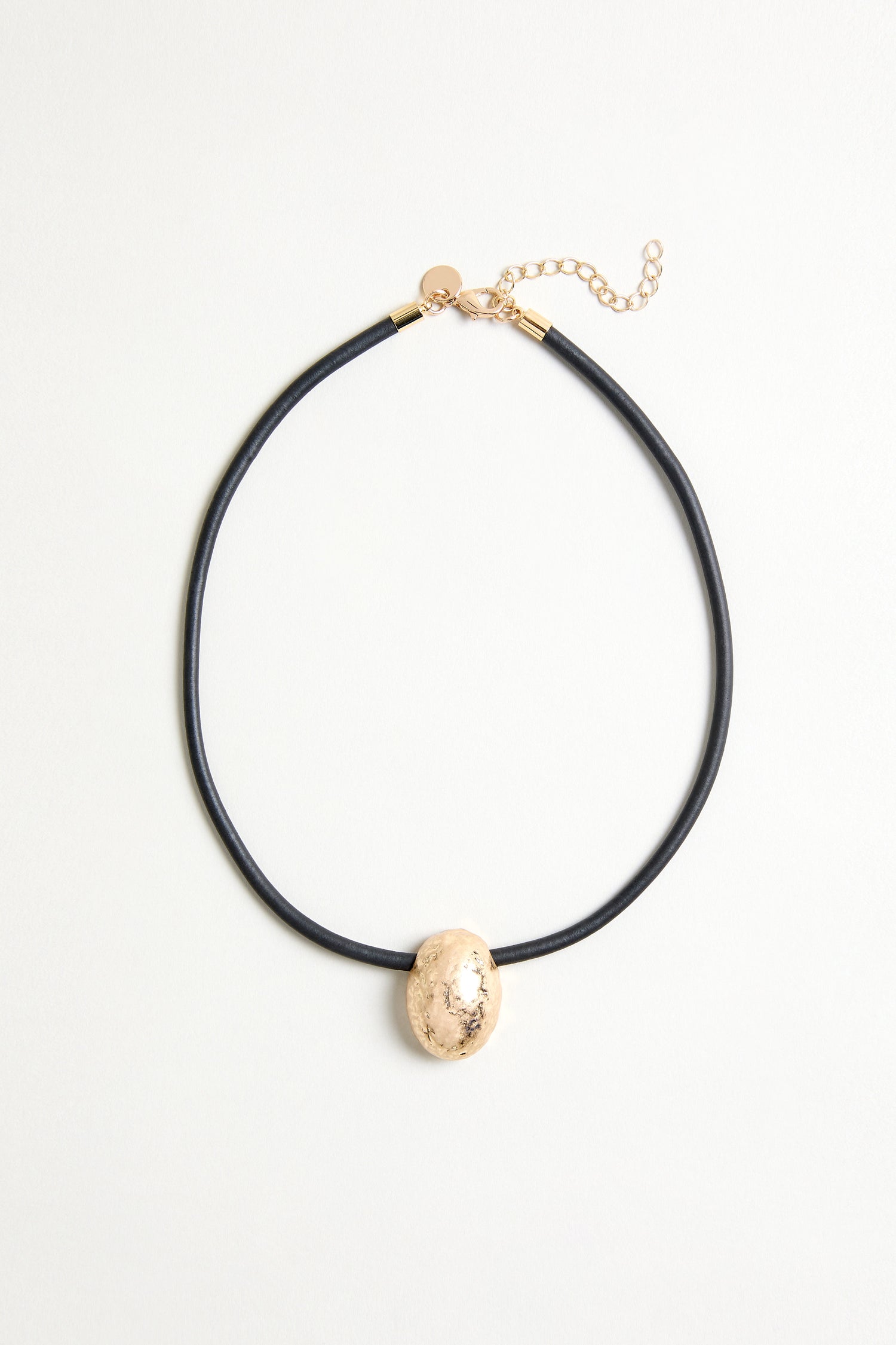 The Hammered Pebble Necklace features a black rubber cord, a single gold hammered pebble-shaped pendant, and an adjustable gold clasp, displayed on a light background.