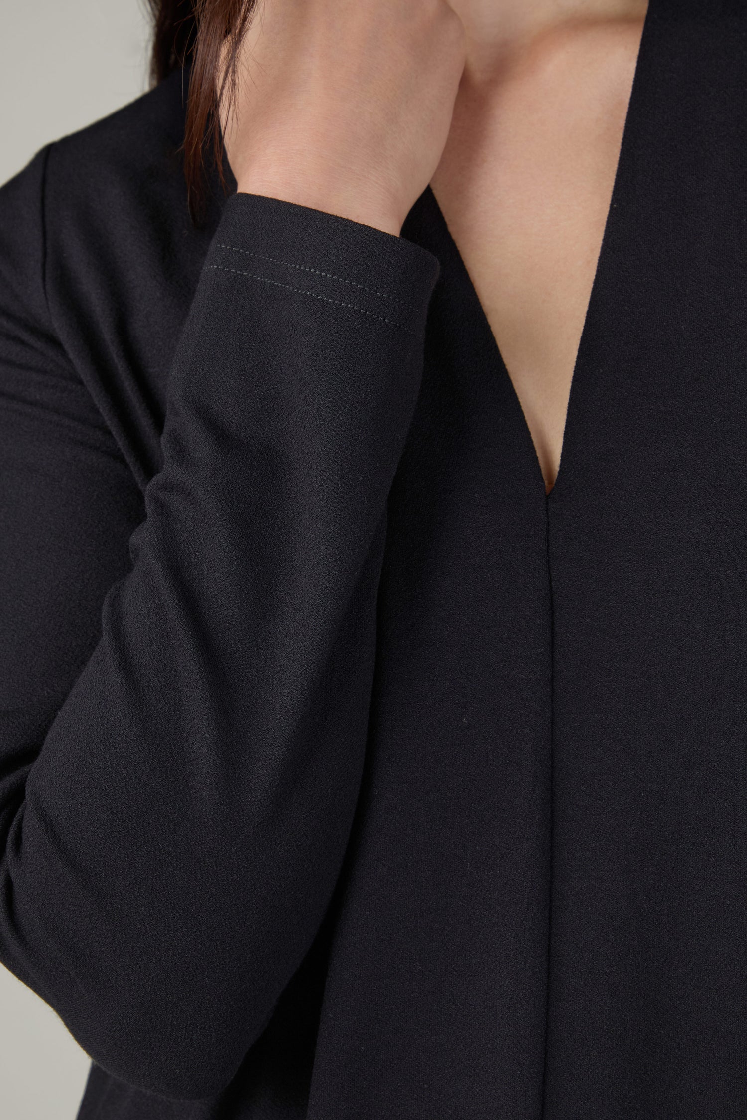 A person wears the Fluid Crepe V Neck Black Bubble Dress, holding a hand near their face, with only the lower face and upper torso visible.