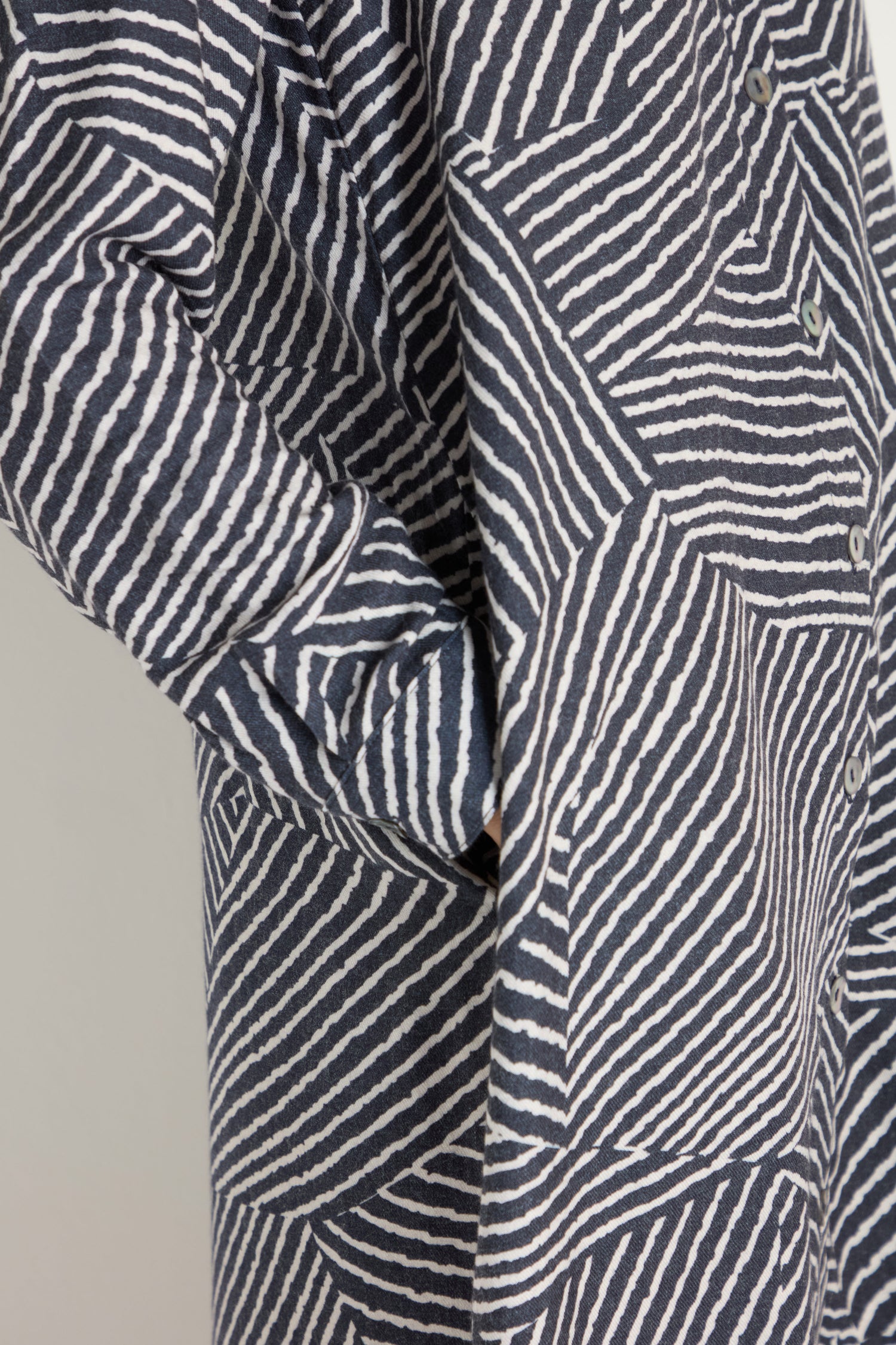 Close-up of a person wearing the Linear Prism Shirt Dress, a buttoned, brushed viscose piece with geometric navy and white stripes and a side pocket. Made in England.