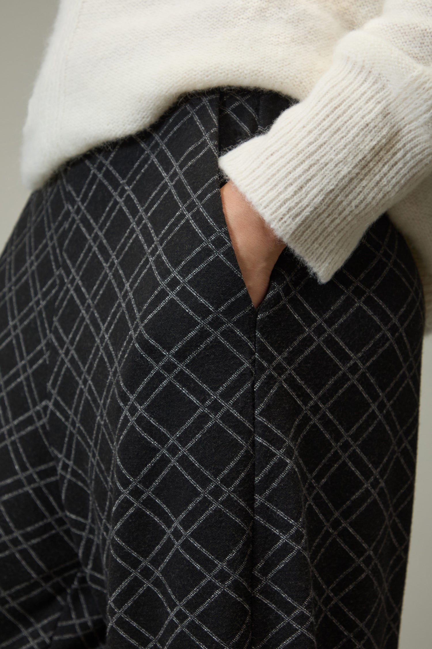 A person wearing a white sweater with their hand in the pocket of Layered Square Jersey Jacquard Trousers, featuring a contemporary grid design.