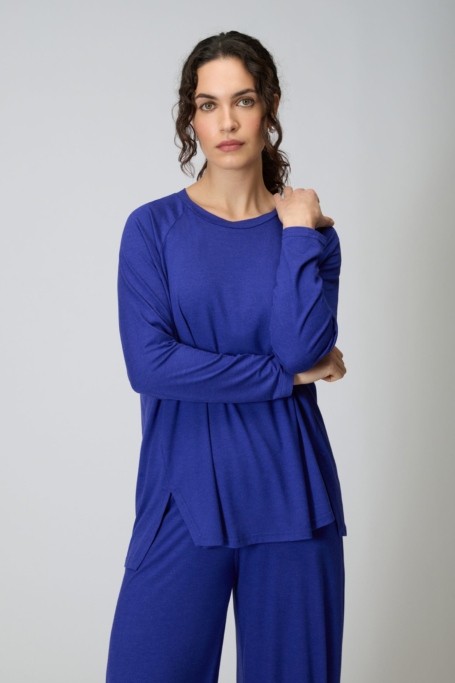 A person wears the Soft Viscose Jersey Boxy Top in blue with matching pants, standing with one arm crossed and the other hand touching their shoulder, looking at the camera.