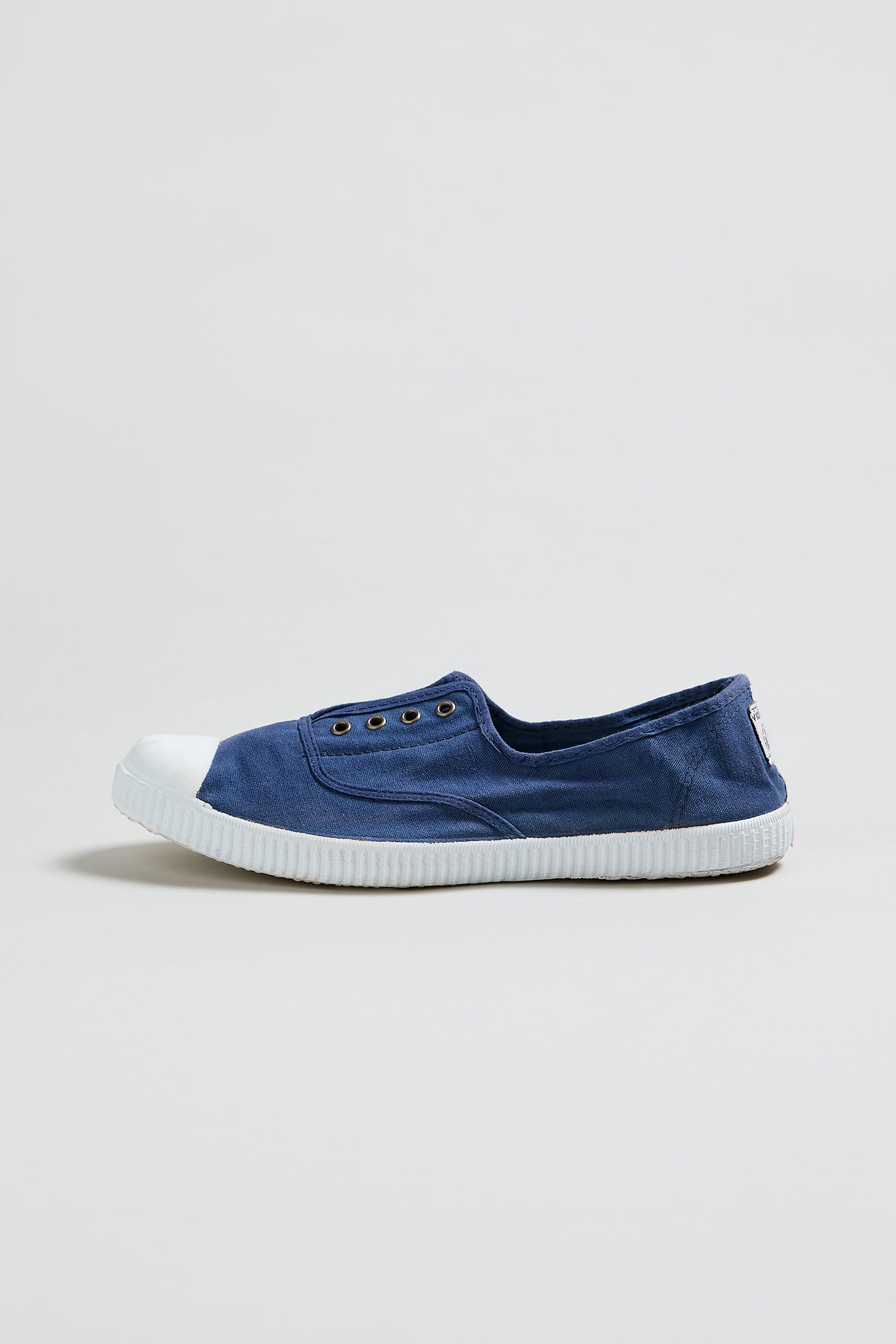 The Inglesa Navy Pumps are canvas slip-on sneakers featuring metal eyelets and a white rubber toe cap and sole, shown in side profile against a plain background.