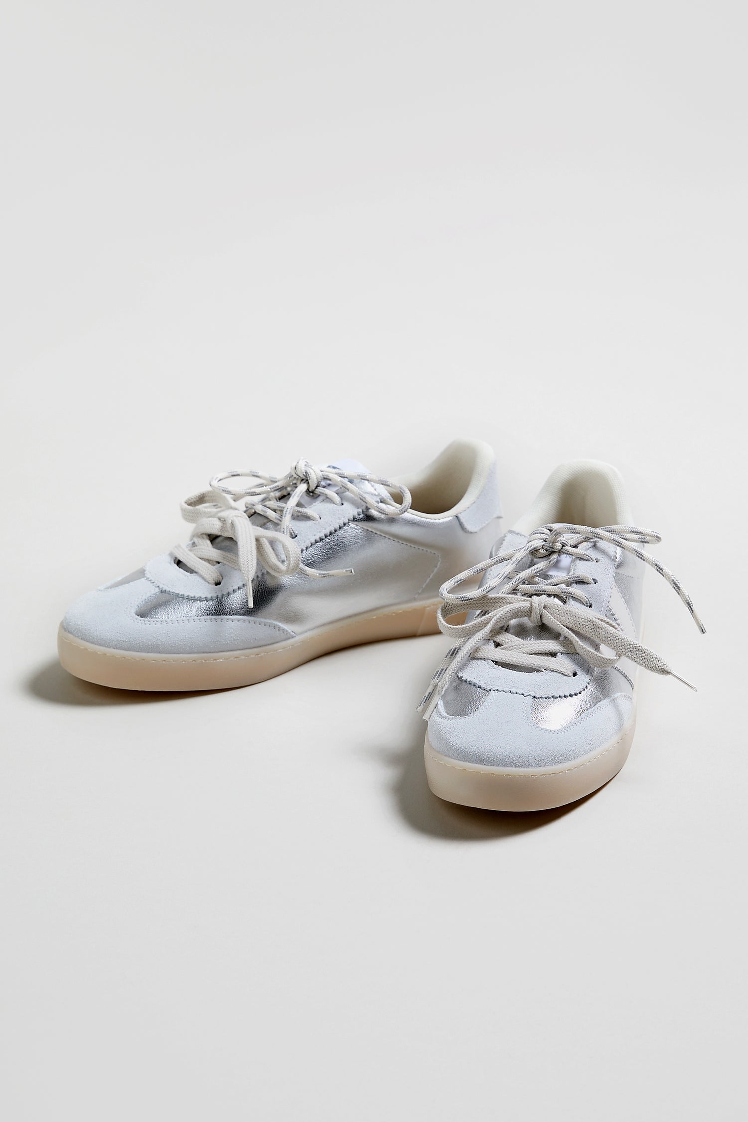 A pair of Berlin Metallic Trainers in white and light gray with white laces and beige rubber soles, displayed on a plain white surface.