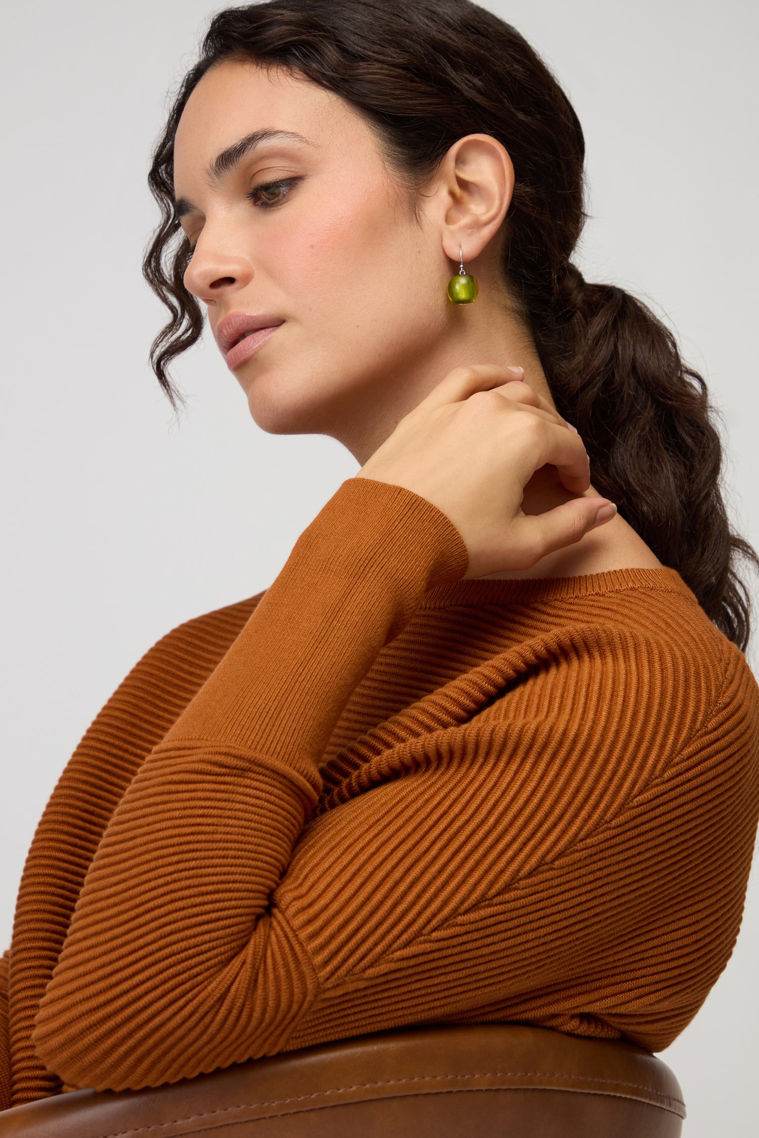 Woman with wavy brown hair in a ponytail, wearing a rust-colored ribbed sweater and Colourful Bead Resin Earrings, seated in profile with her hand near her neck.