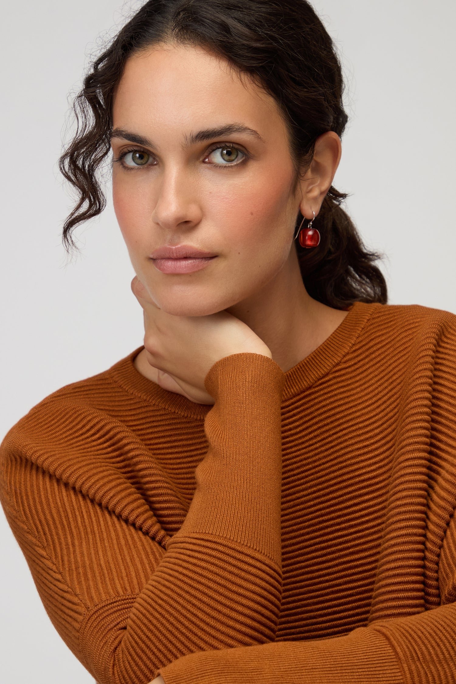 A woman with wavy dark hair wears Colourful Bead Resin Earrings and a rust ribbed sweater, resting her chin on her hand as she looks at the camera against a neutral background.