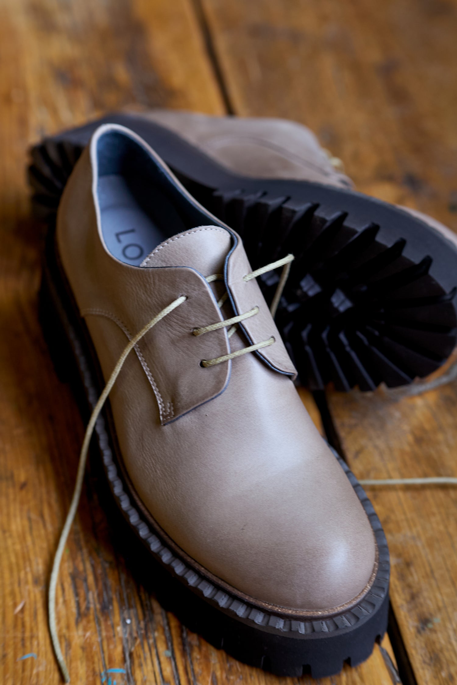 A pair of Two Tone Lace Up Leather Brogues with thick black soles, crafted from beige and black leather, placed on a wooden floor.