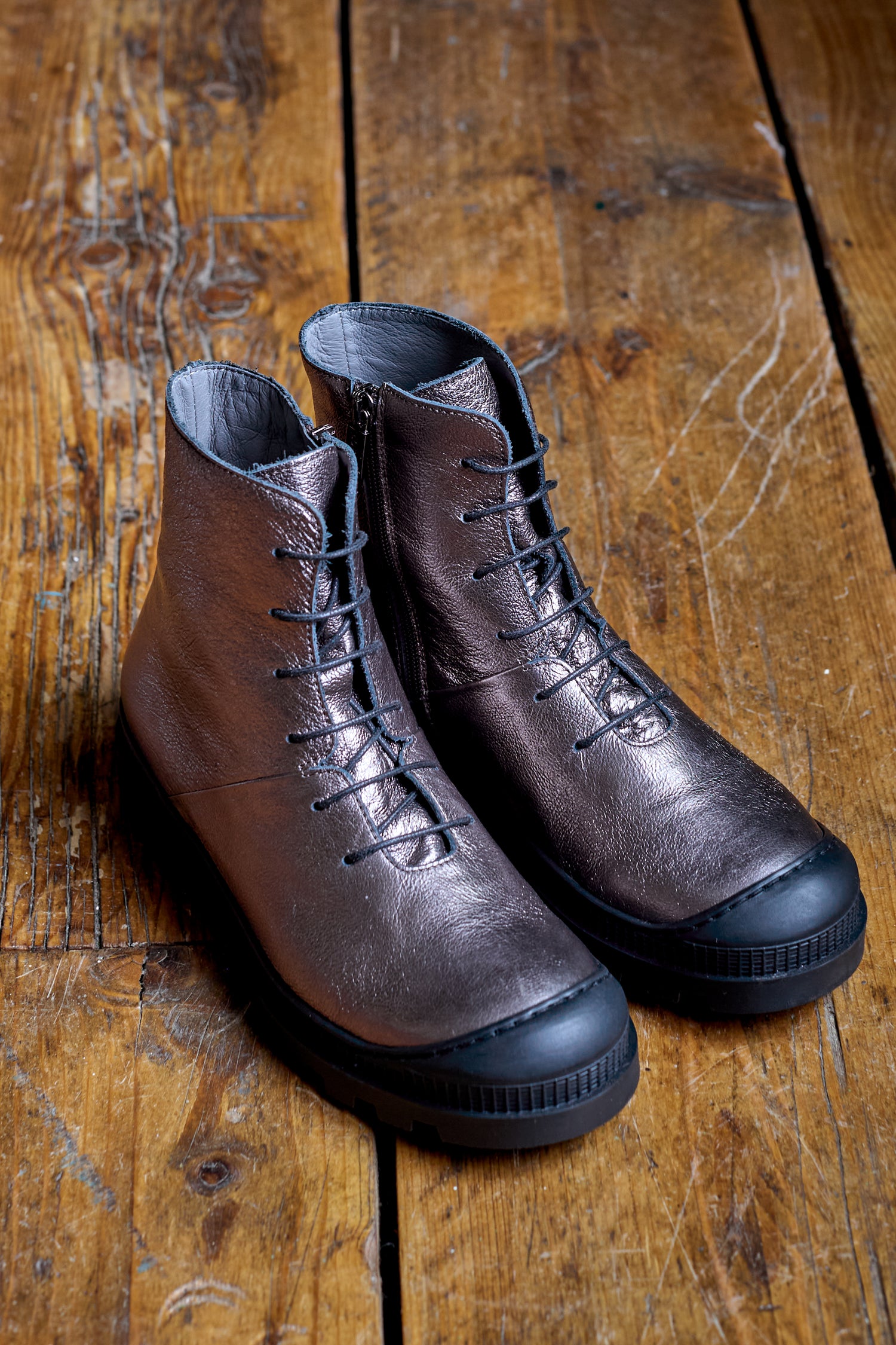 A pair of Rose Metallic Lace Up Leather Boots made from high-grade leather with black rubber soles, placed on a wooden floor.