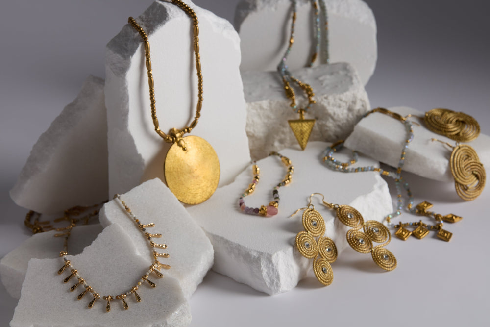 Colorful, abstract metal jewelry pieces displayed on textured white stones against a gray background.