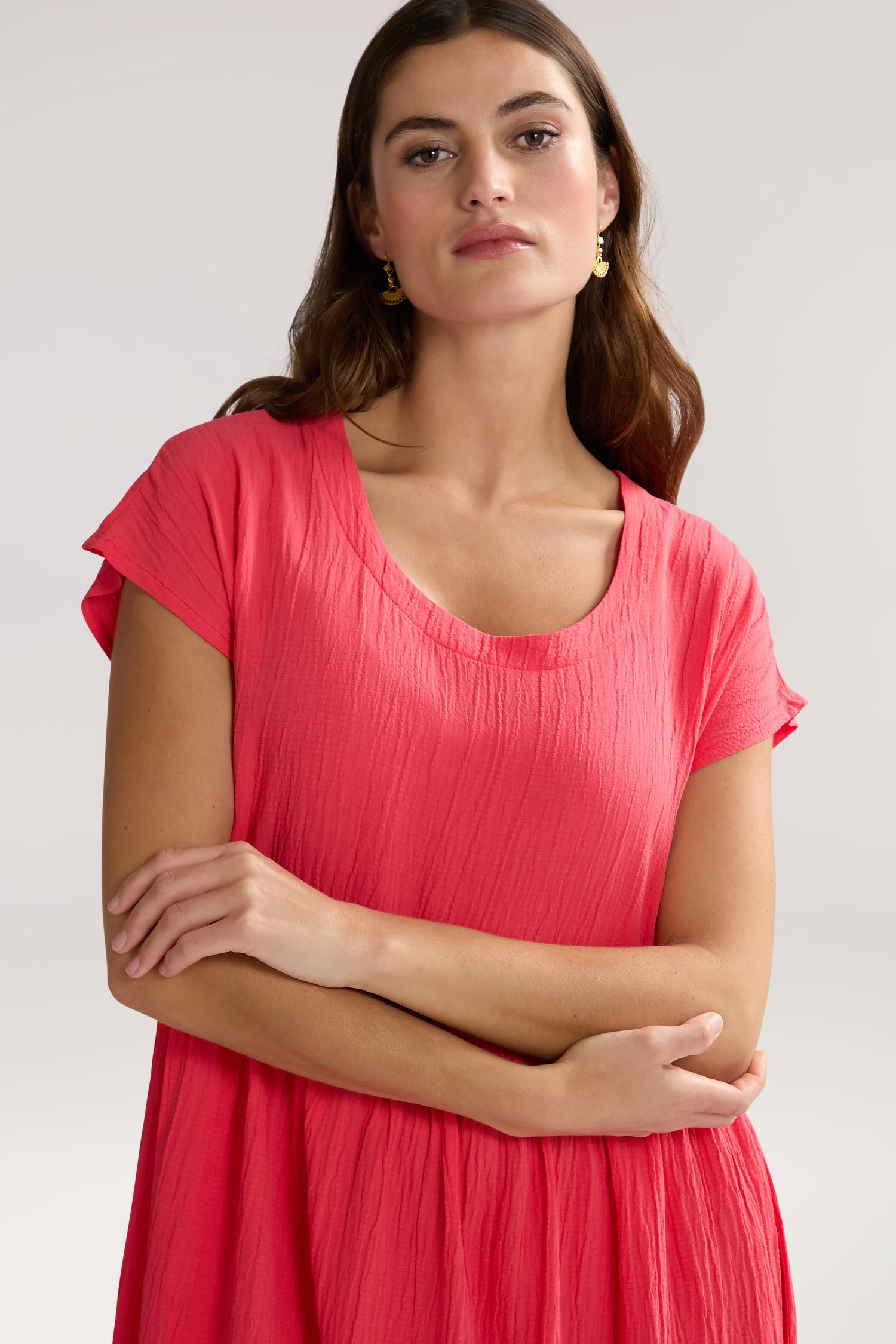 A woman with long hair wearing a bright pink Crinkle Viscose Bubble Dress, arms crossed, looks into the camera against a plain background.