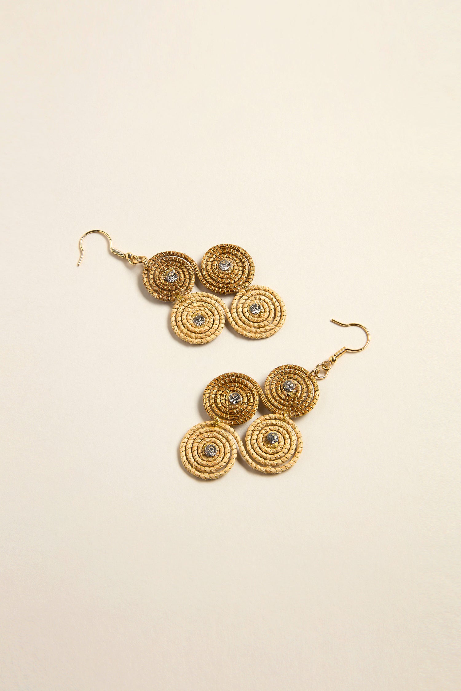 Golden Grass Woven Spiral Rhinestone Earrings, featuring three circular designs with central gemstones, are beautifully displayed on a light beige background. These sustainable pieces combine art and nature, showcasing a passion for thoughtful design.