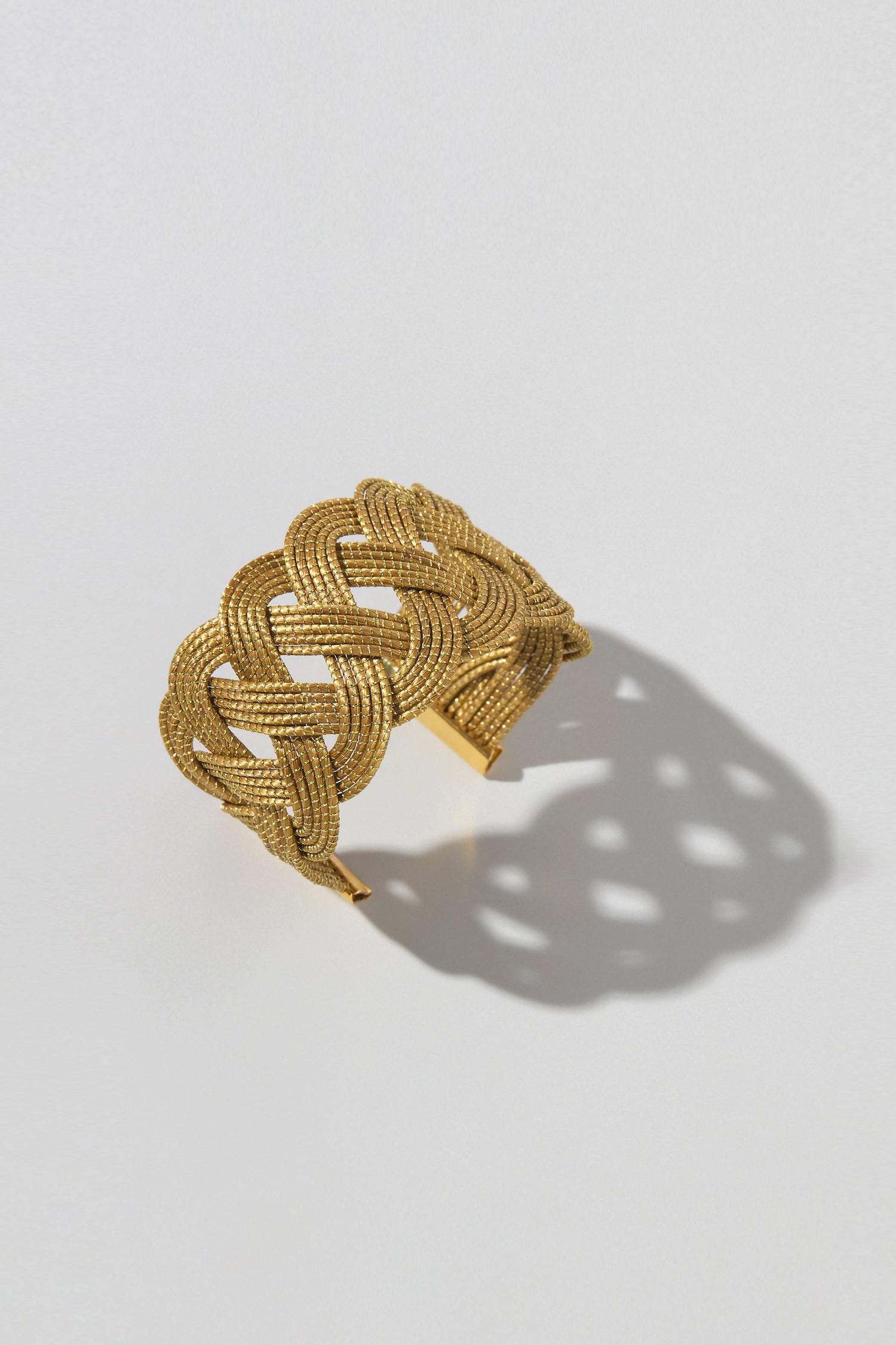 The Golden Grass Woven Bracelet, with its intricate artisanal design, casts a shadow on a light surface.