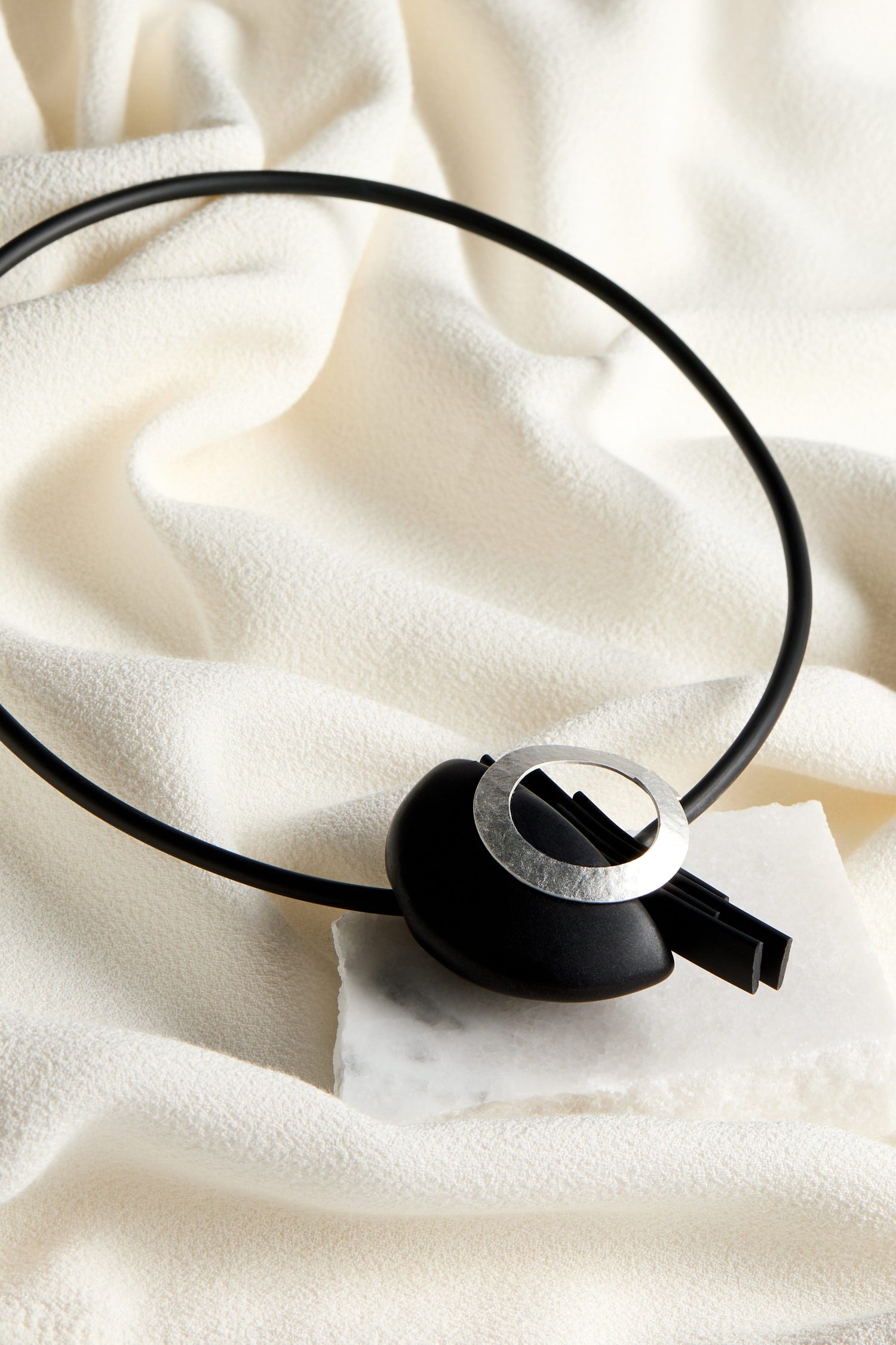 A black and white Saturn Necklace made with magnetic beads on a white surface.