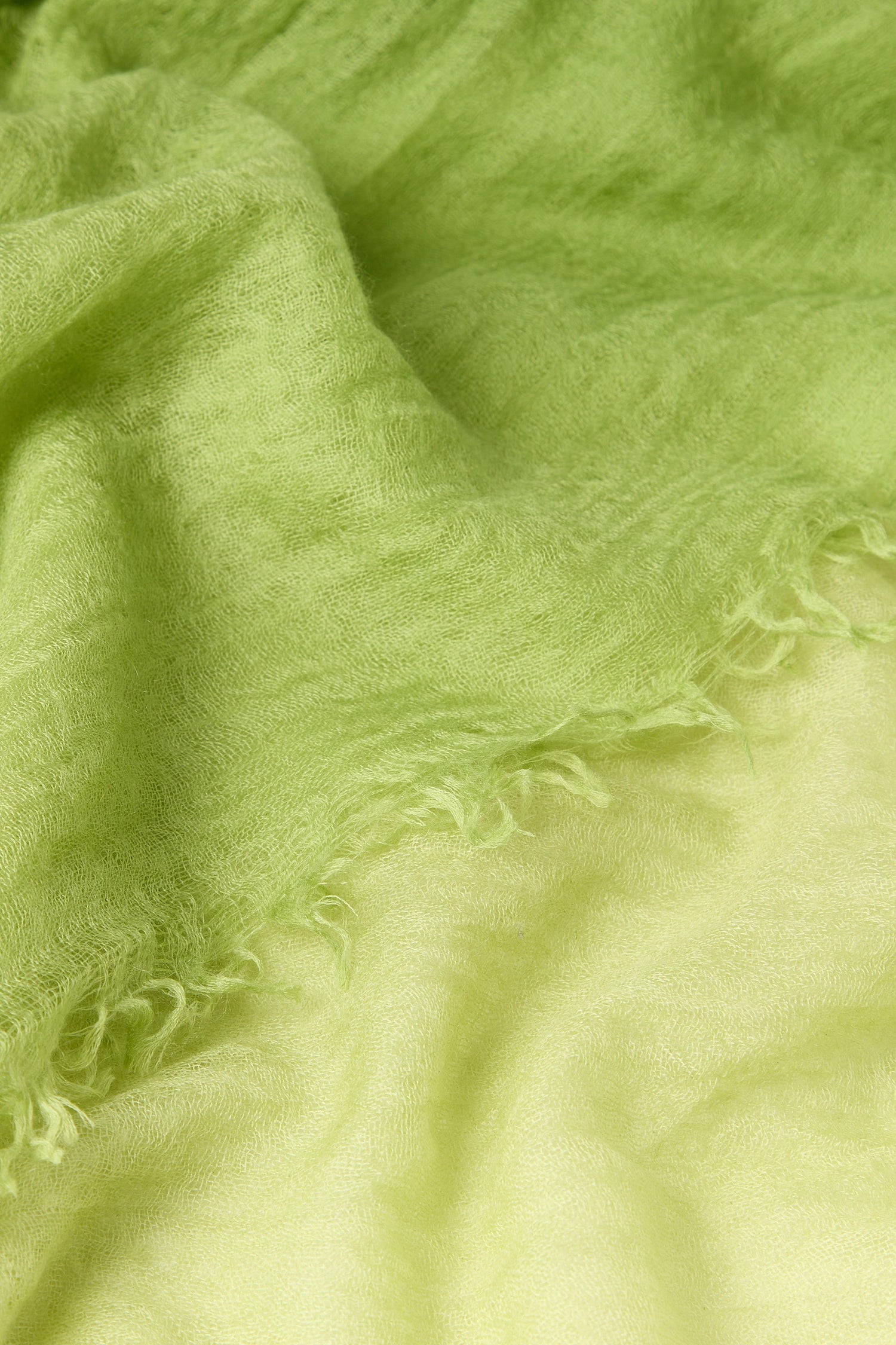 Close-up of a soft green textured fabric with frayed edges, showcasing its delicate surface. This could be part of an exquisite Ombre Cashmere Scarf, adding a touch of elegance to your outfit.