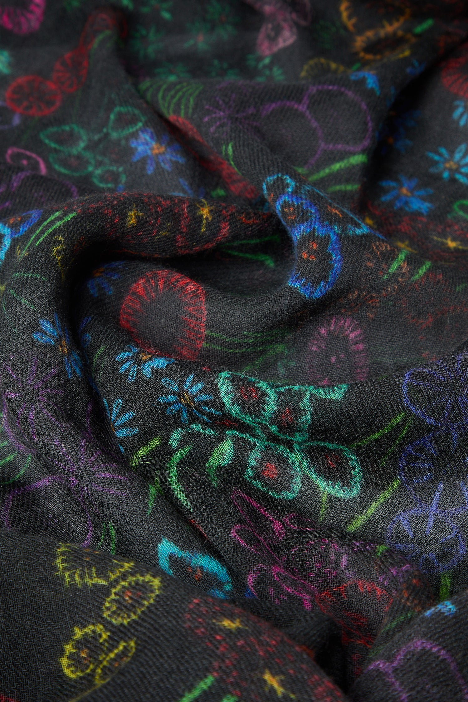 Here's a close-up of the Winter Floral Wool Scarf in black fabric, adorned with vibrant floral embroidery showcasing detailed patterns in red, green, blue, and yellow. The material is slightly wrinkled and is part of our premium Winter Floral Wool Scarf collection.