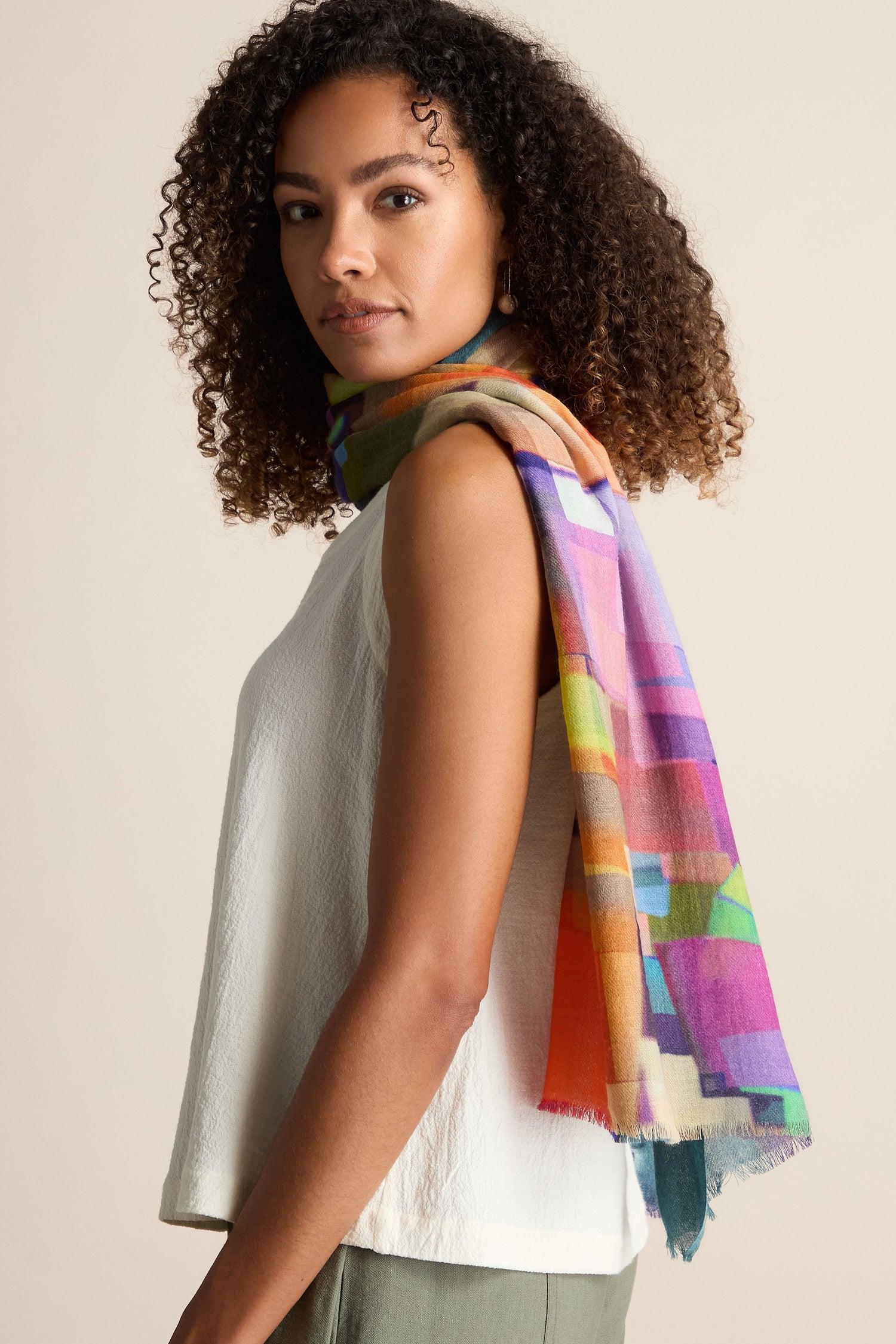 A person wearing a white sleeveless top and a vibrant Square Collage Wool Scarf draped over their shoulder stands against a plain background.