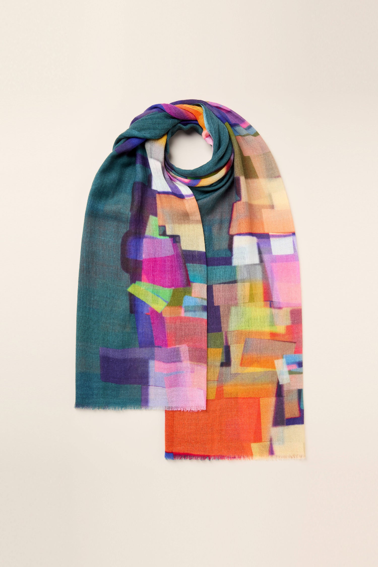 The Square Collage Wool Scarf is adorned with an abstract geometric pattern in shades of teal, pink, orange, and purple on a light background.